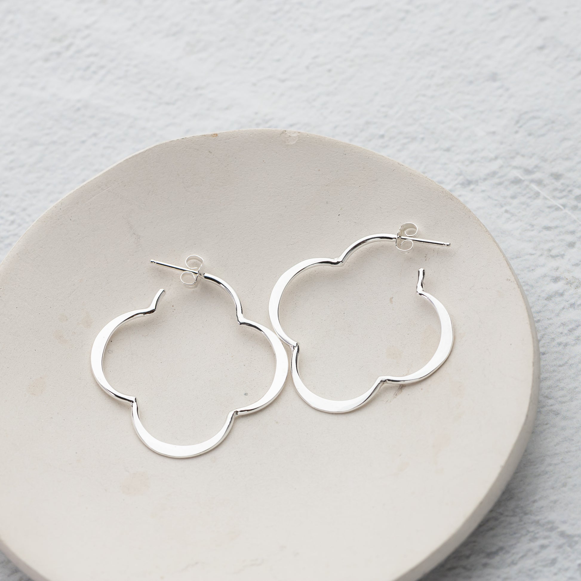 unique handmade sterling silver hoop earrings on a round stone surface with a light gray background