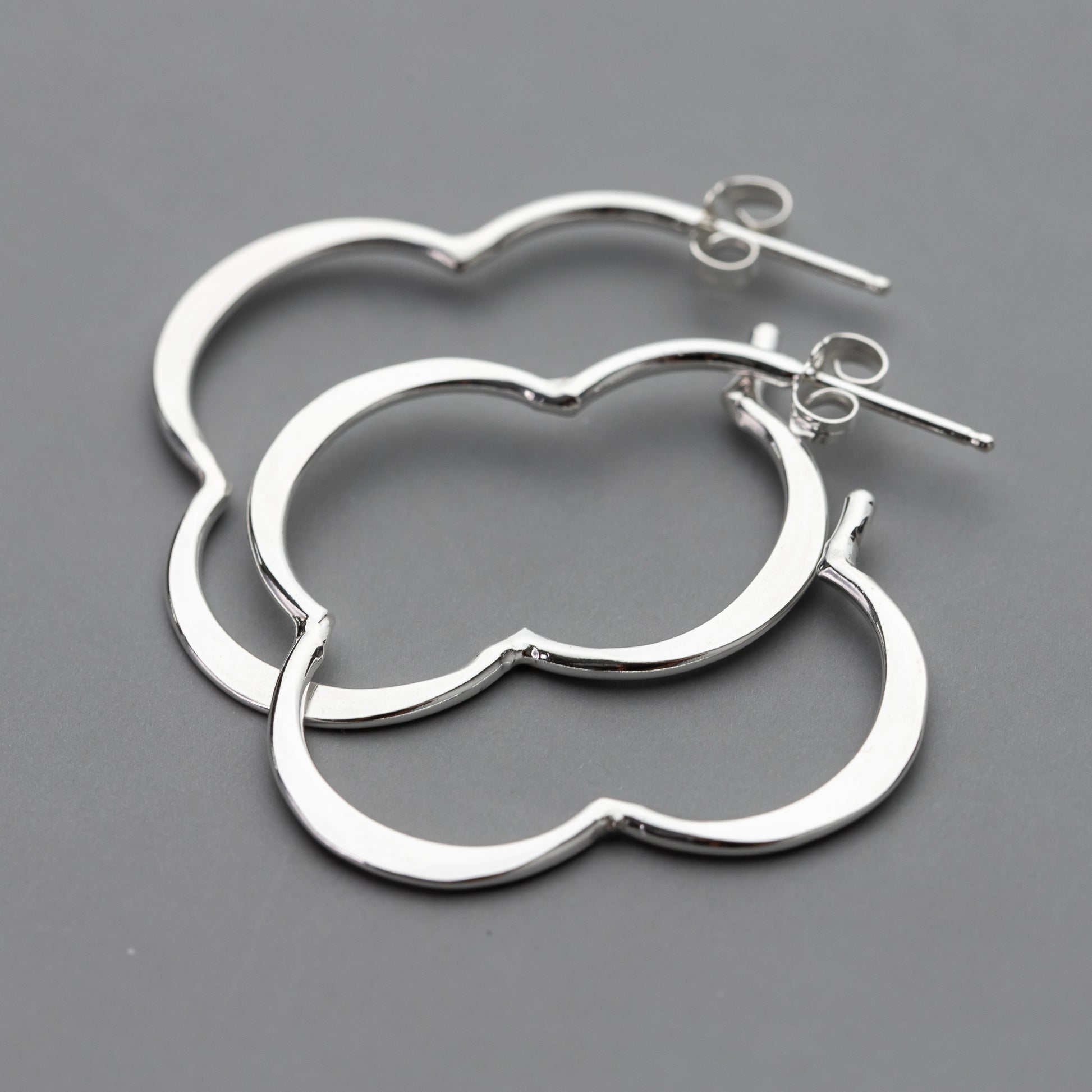 Pair of handmade silver post hoop earrings in a unique clover shape on a gray background