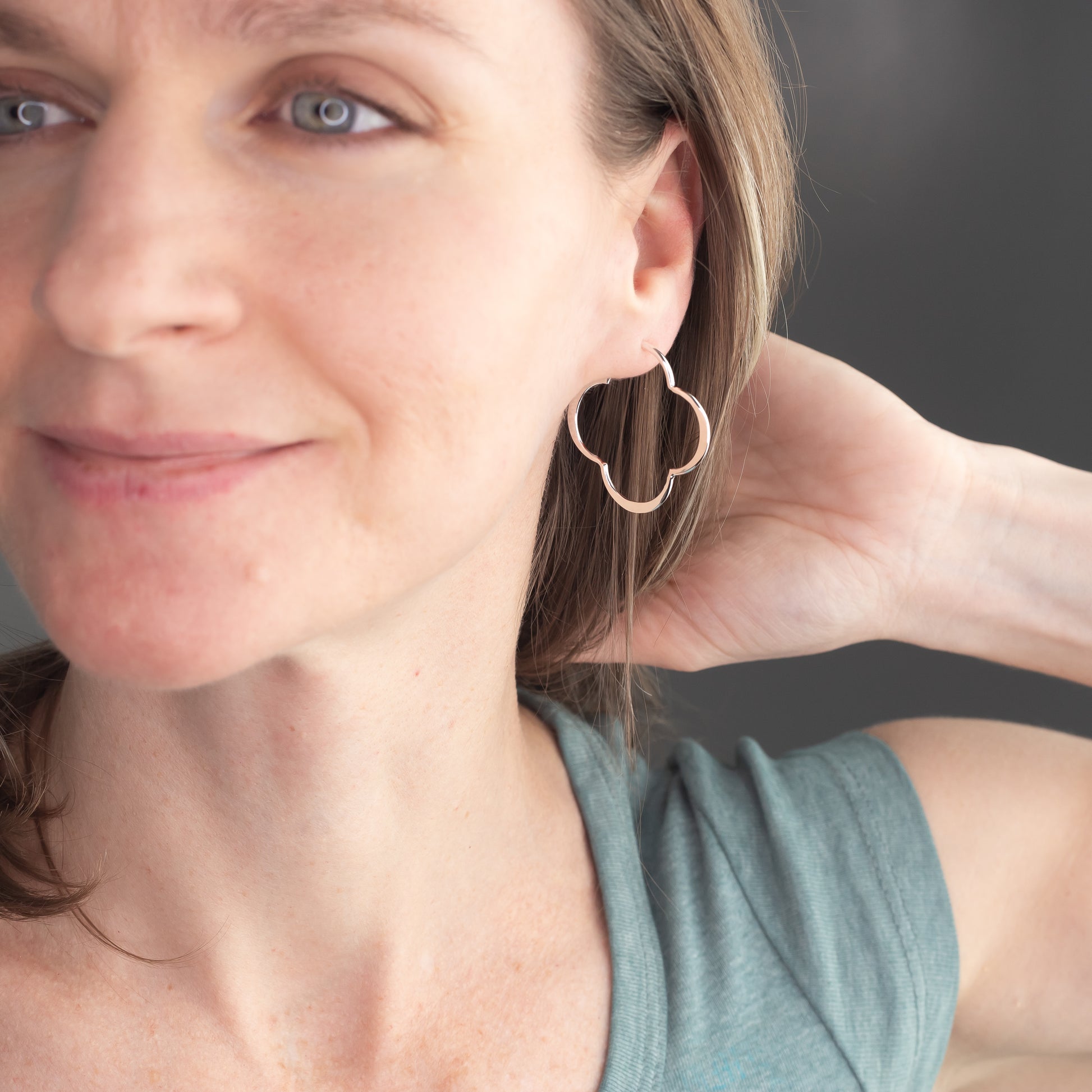 Woman wearing sterling silver clover shaped hoop earrings with a neutral background