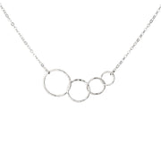 A silver necklace featuring four interlocking, open circular rings of varying sizes on a delicate silver cable chain, shown against a plain white background.