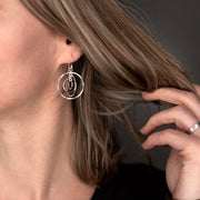 A close-up lifestyle shot of a woman wearing a silver multi-hoop dangle earring, with her hand touching her hair against a dark gray background.