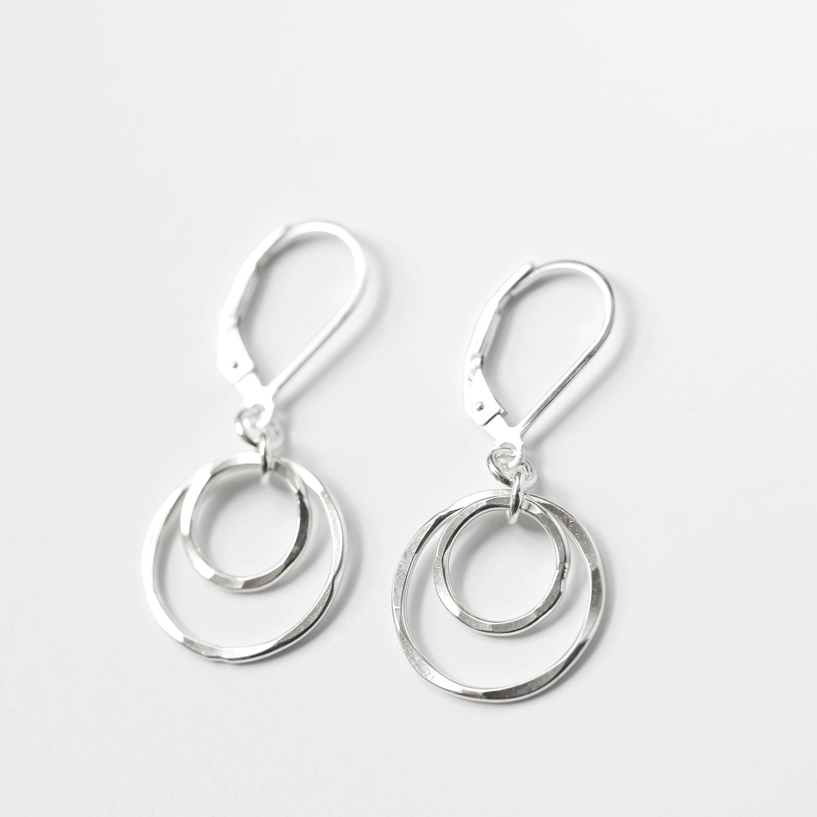 A pair of silver double-ring dangle earrings with leverback closures, shown on a clean light gray background.