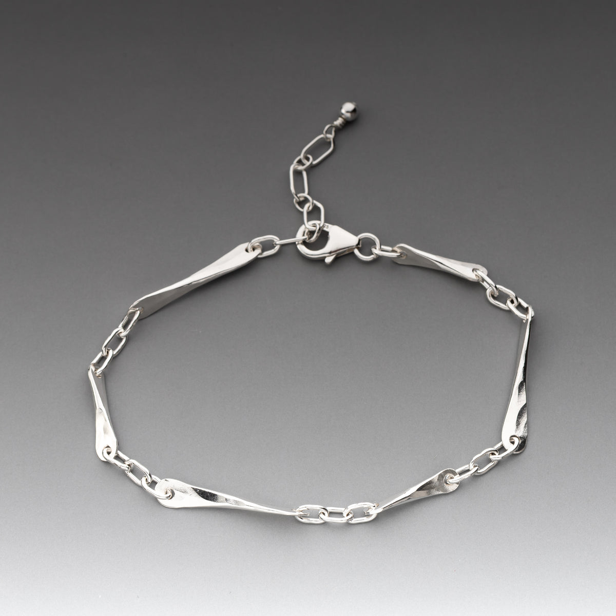 A polished sterling silver link bracelet with alternating flat polished bars and oval chain links, displayed on a dark gray gradient background.