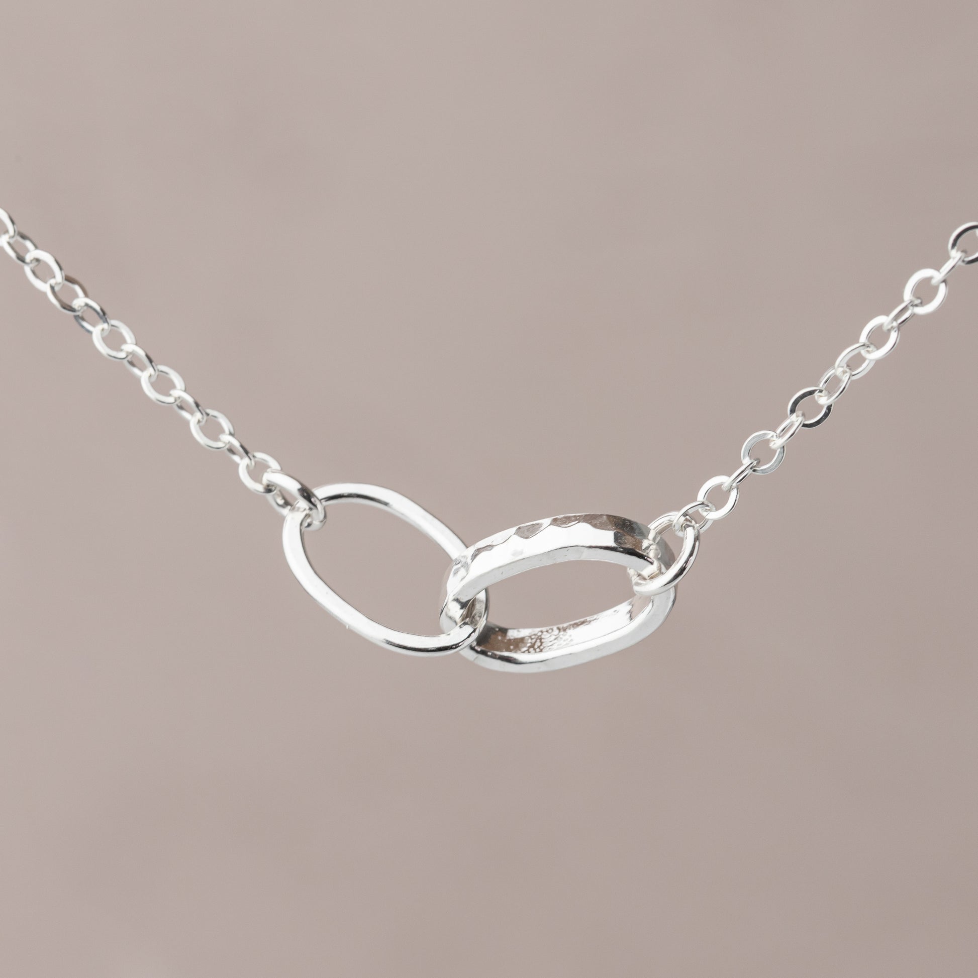 Silver necklace with an interlocking oval thick and thin link design on a beige background