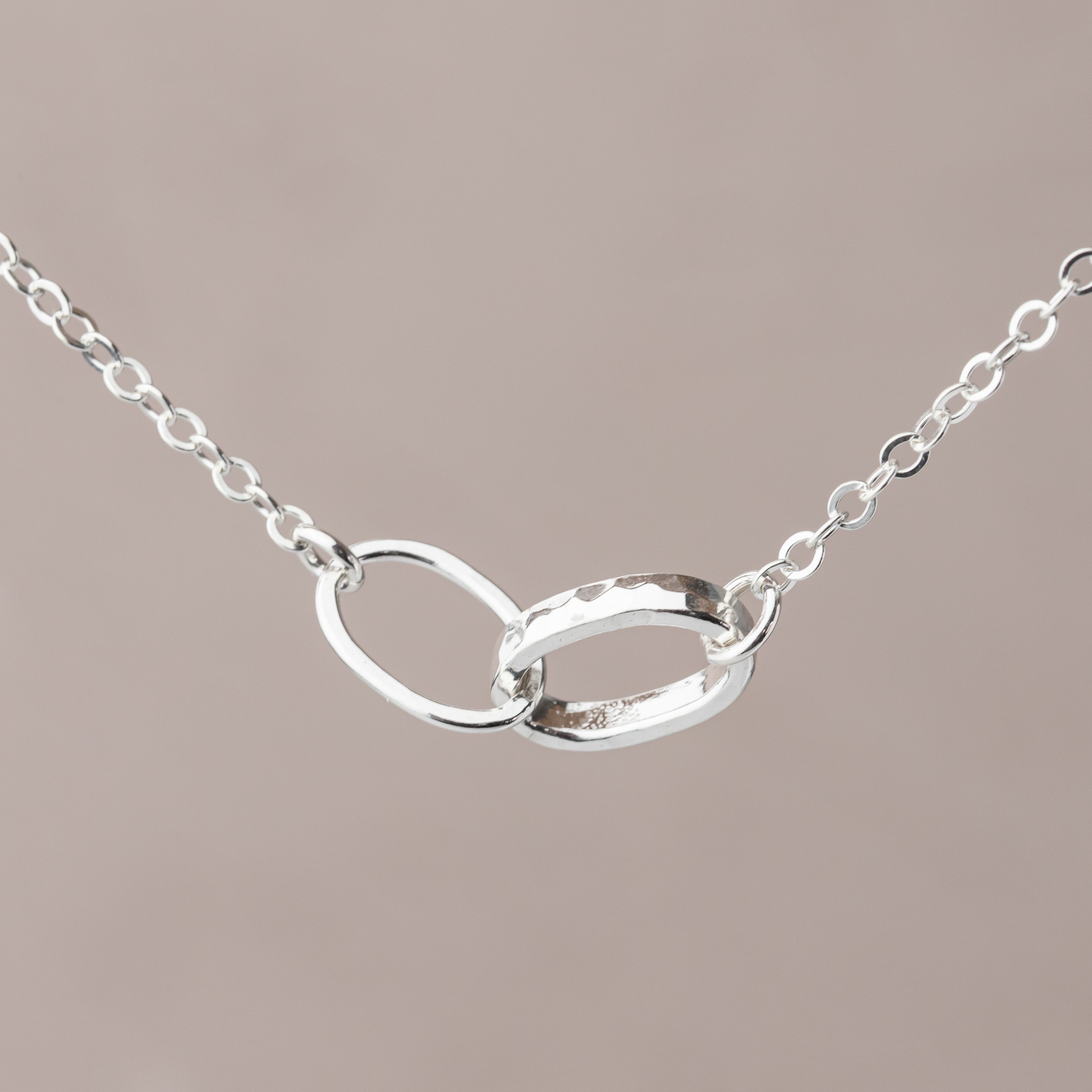 Silver necklace with an interlocking oval thick and thin link design on a beige background