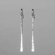 A pair of sterling silver drop earrings with a hammered finish and fishhook backings, displayed against a solid gray background. Handmade by Lizardi Jewelry