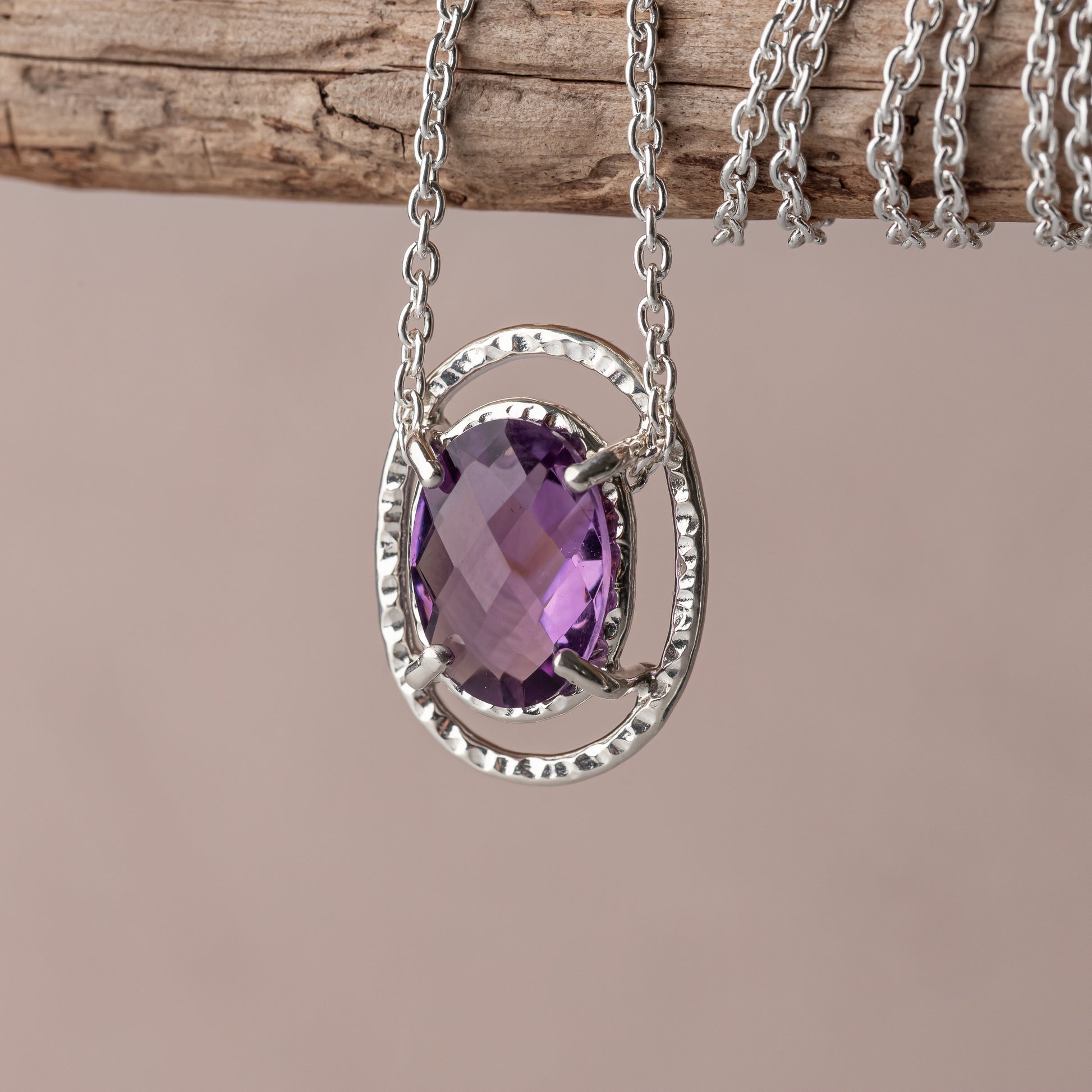 Silver necklace with a purple amethyst gemstone pendant on a wooden surface