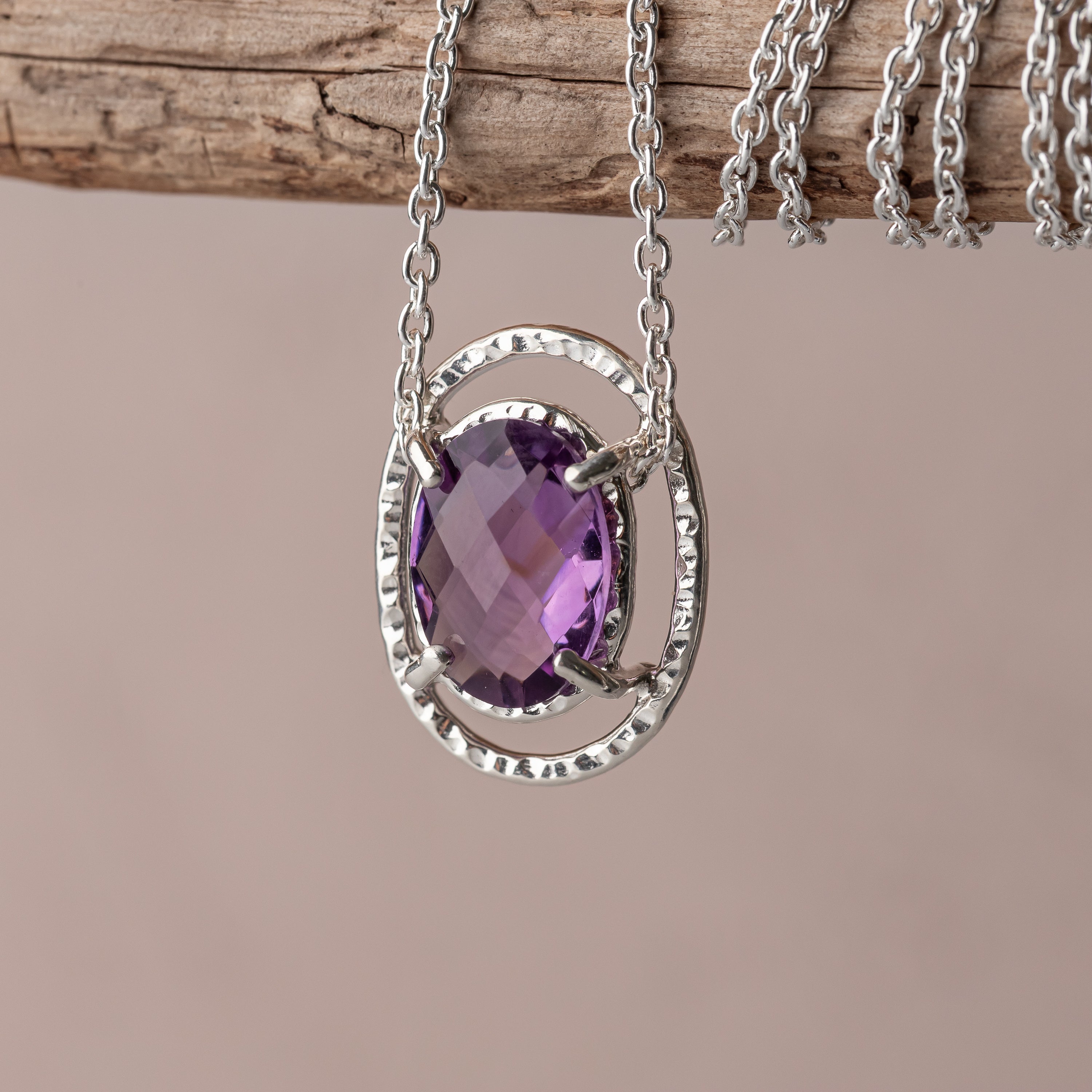Silver necklace with a purple amethyst gemstone pendant on a wooden surface