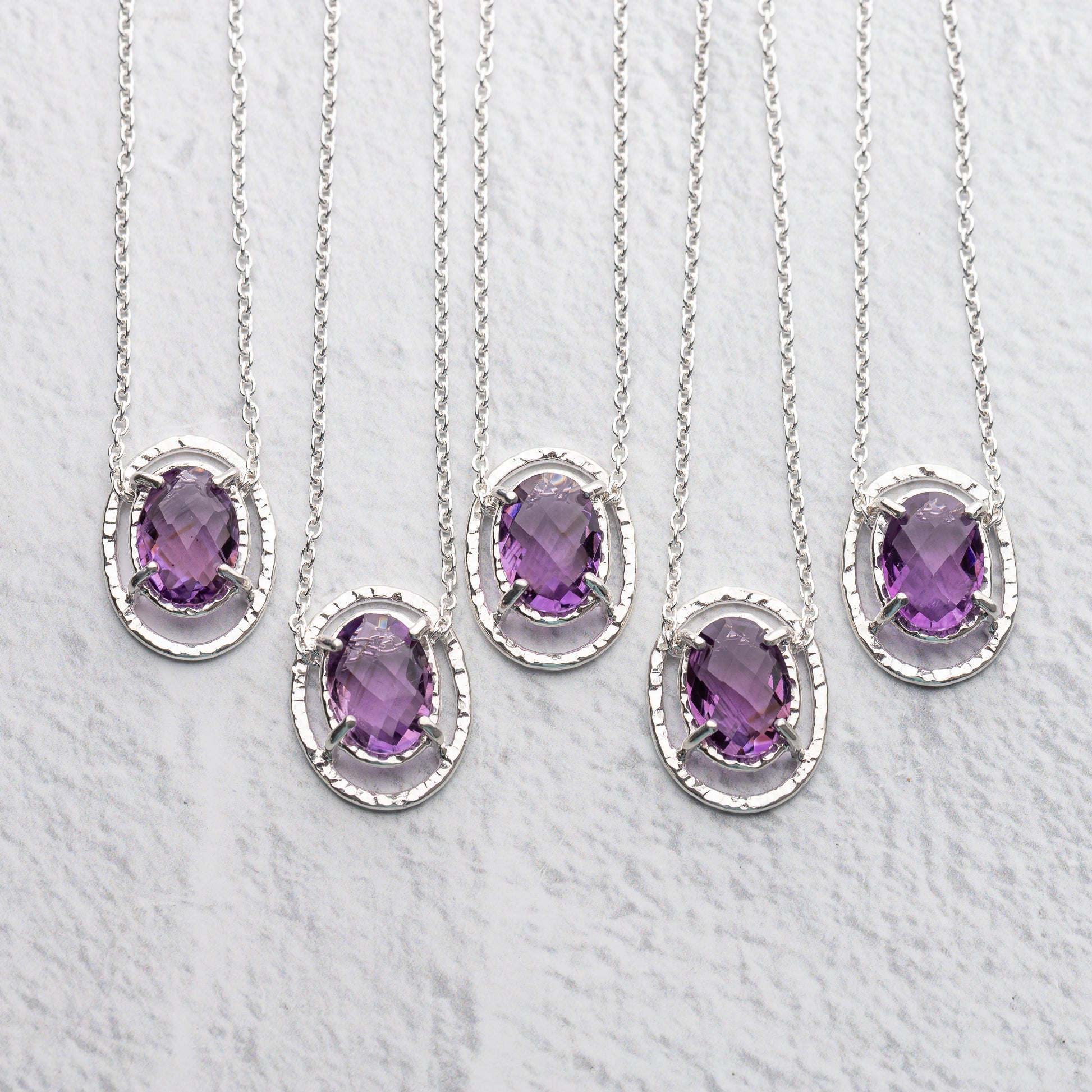 Set of five silver necklaces with purple amethyst gemstones on a light gray background