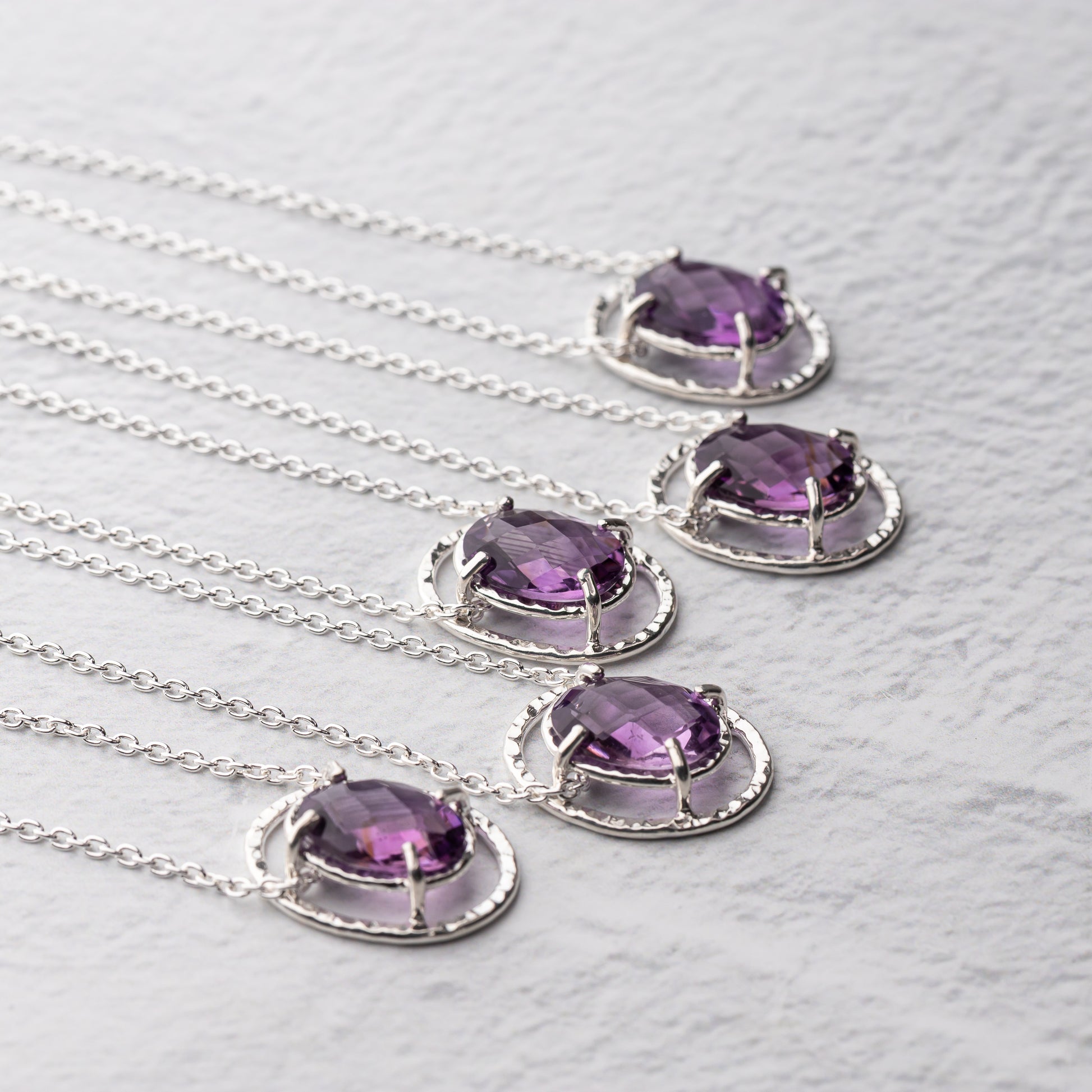 Silver necklaces with purple amethyst gemstones on a textured white surface