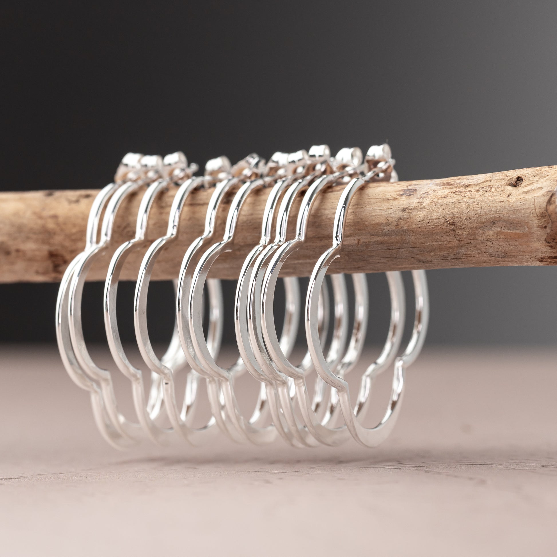 Silver clover shaped hoop earrings on a wooden rod with a neutral background