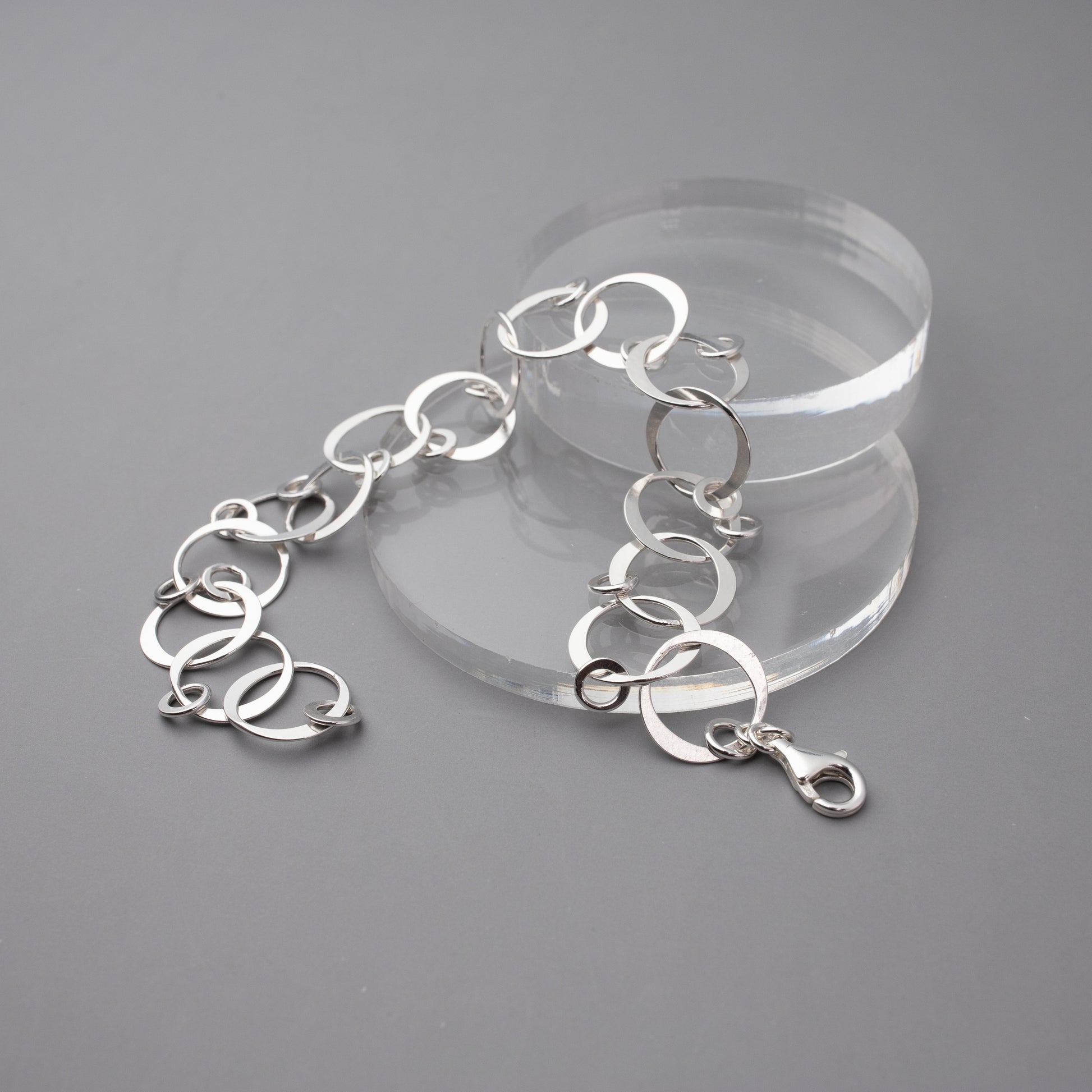 Silver bracelet on a clear stand against a gray background.  The bracelet is handmade hammered sterling silver links to create a chain with tiny silver circle dangles on each link