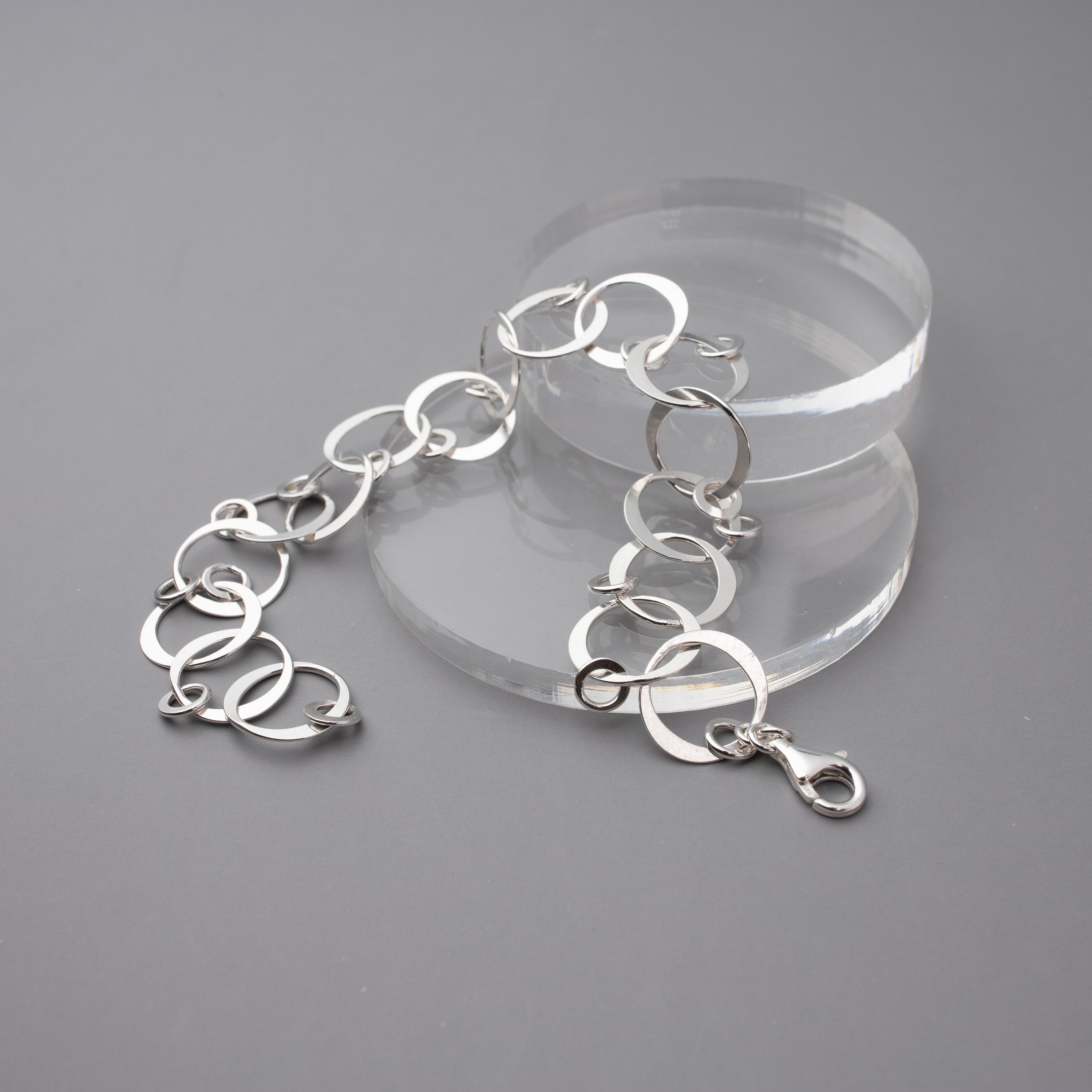 Silver bracelet on a clear stand against a gray background.  The bracelet is handmade hammered sterling silver links to create a chain with tiny silver circle dangles on each link