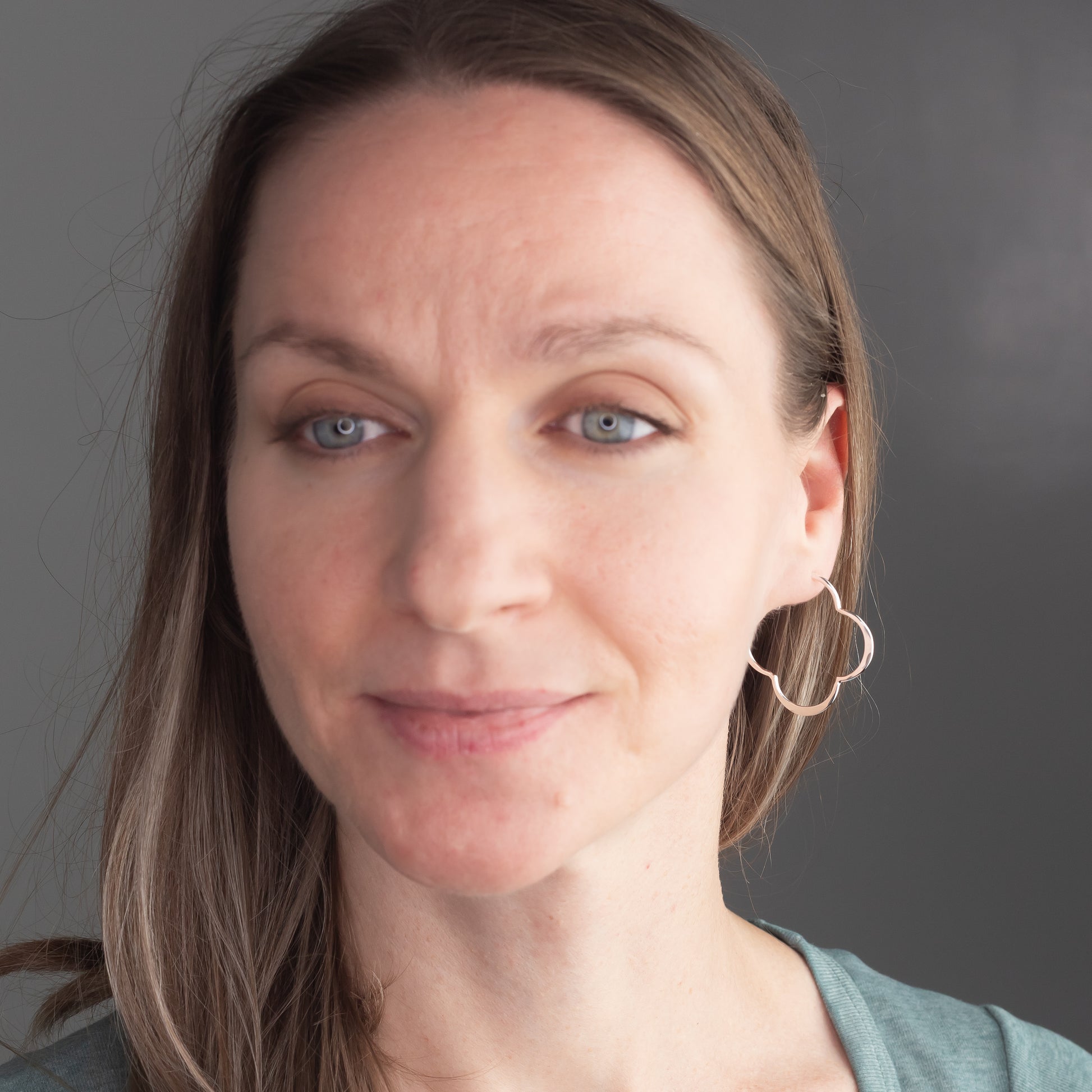 Close-up of a woman with unique sterling silver hoop earrings against a gray background
