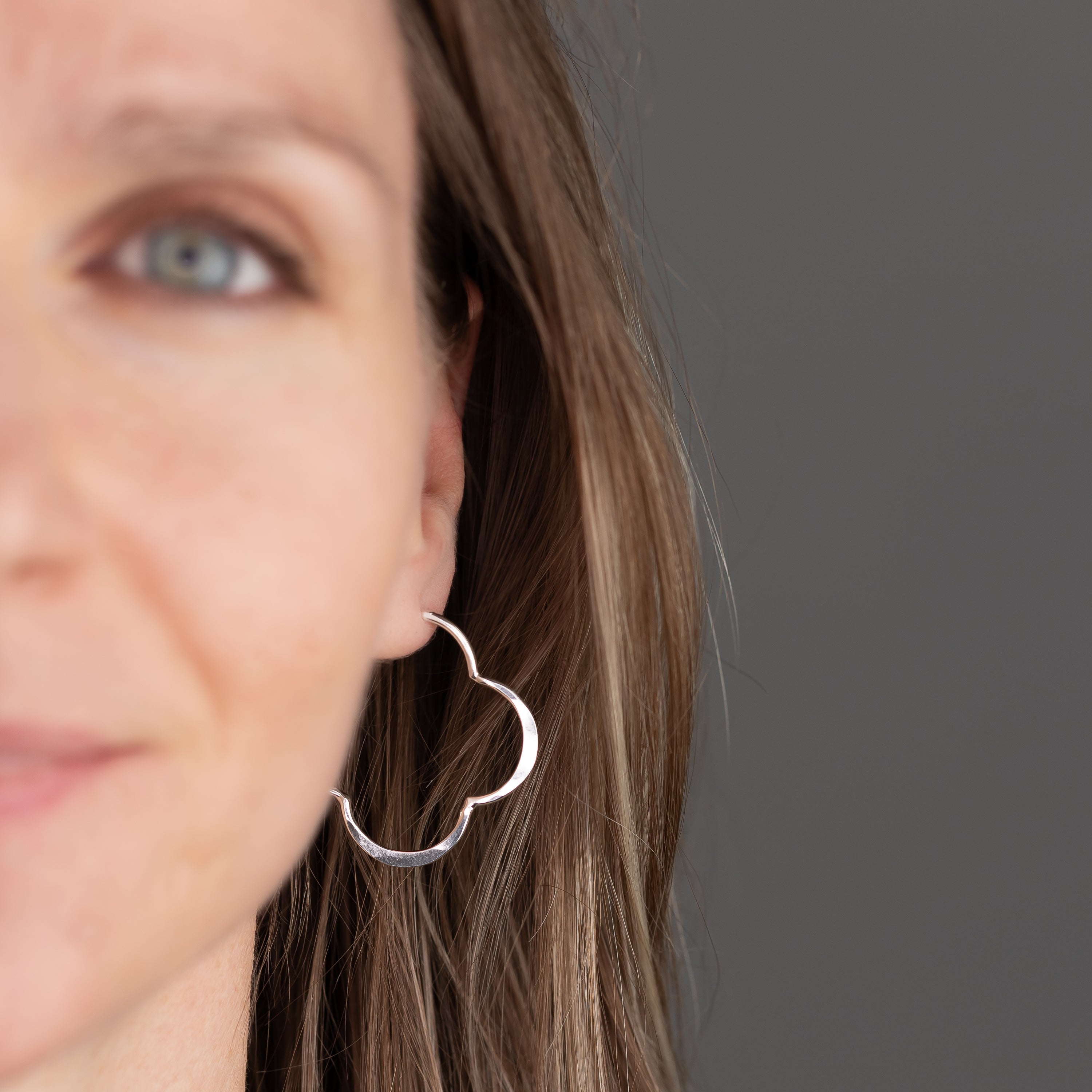 Close-up of a person wearing a unique sterling silver hoop earring against a gray background