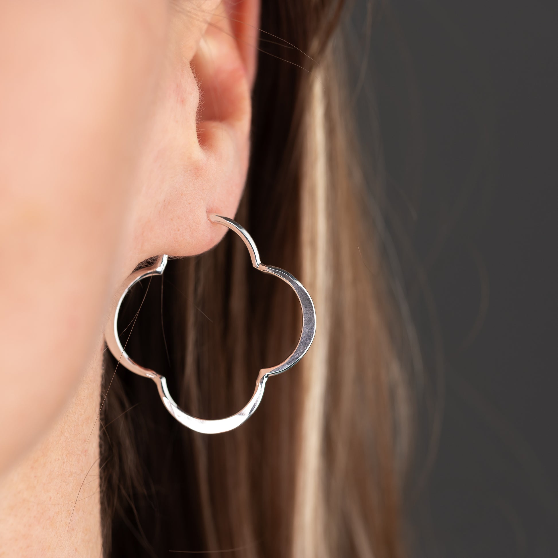 handmade Silver post hoop earring in a unique clover shape worn by a person with a neutral background