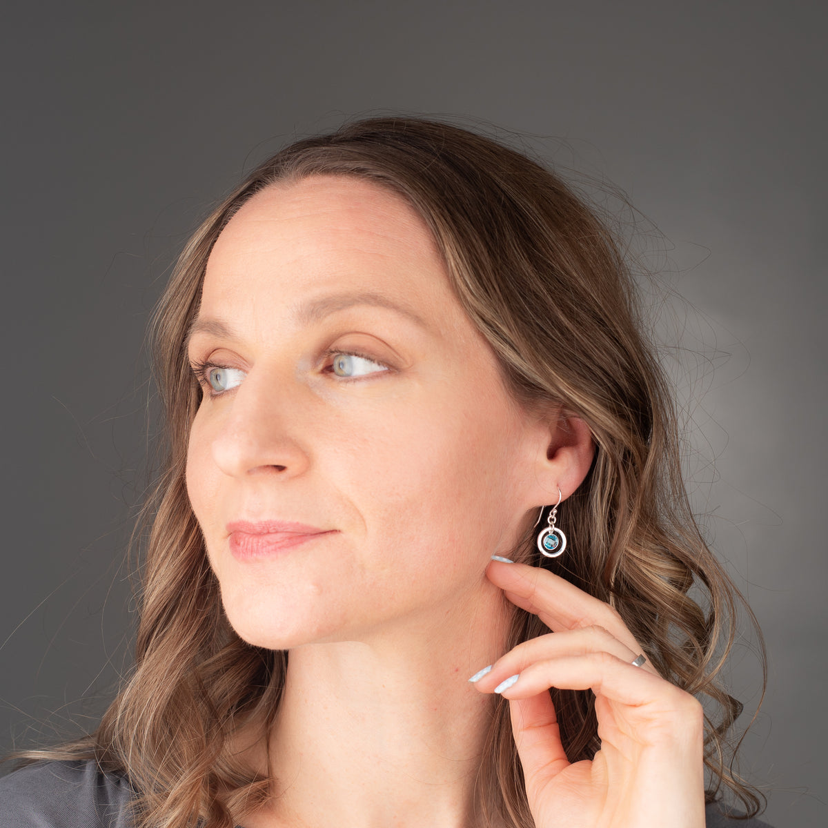 handmade sterling silver birthstone earrings shown on a model.  They are dainty and minimalist with a hammered circle frame and sparkling cubic zirconia gemstones
