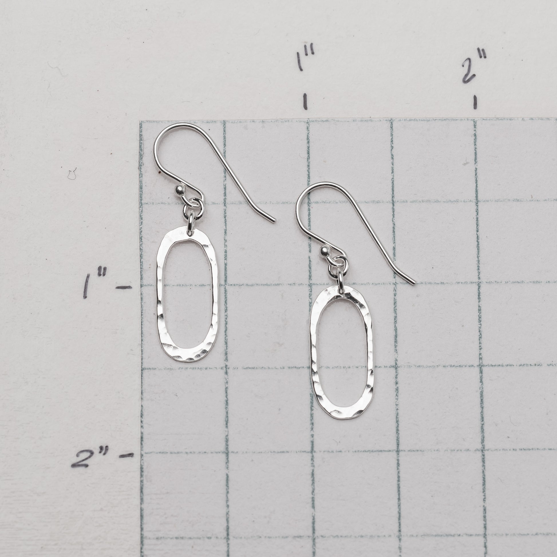 Silver oval earrings on a gray grid background