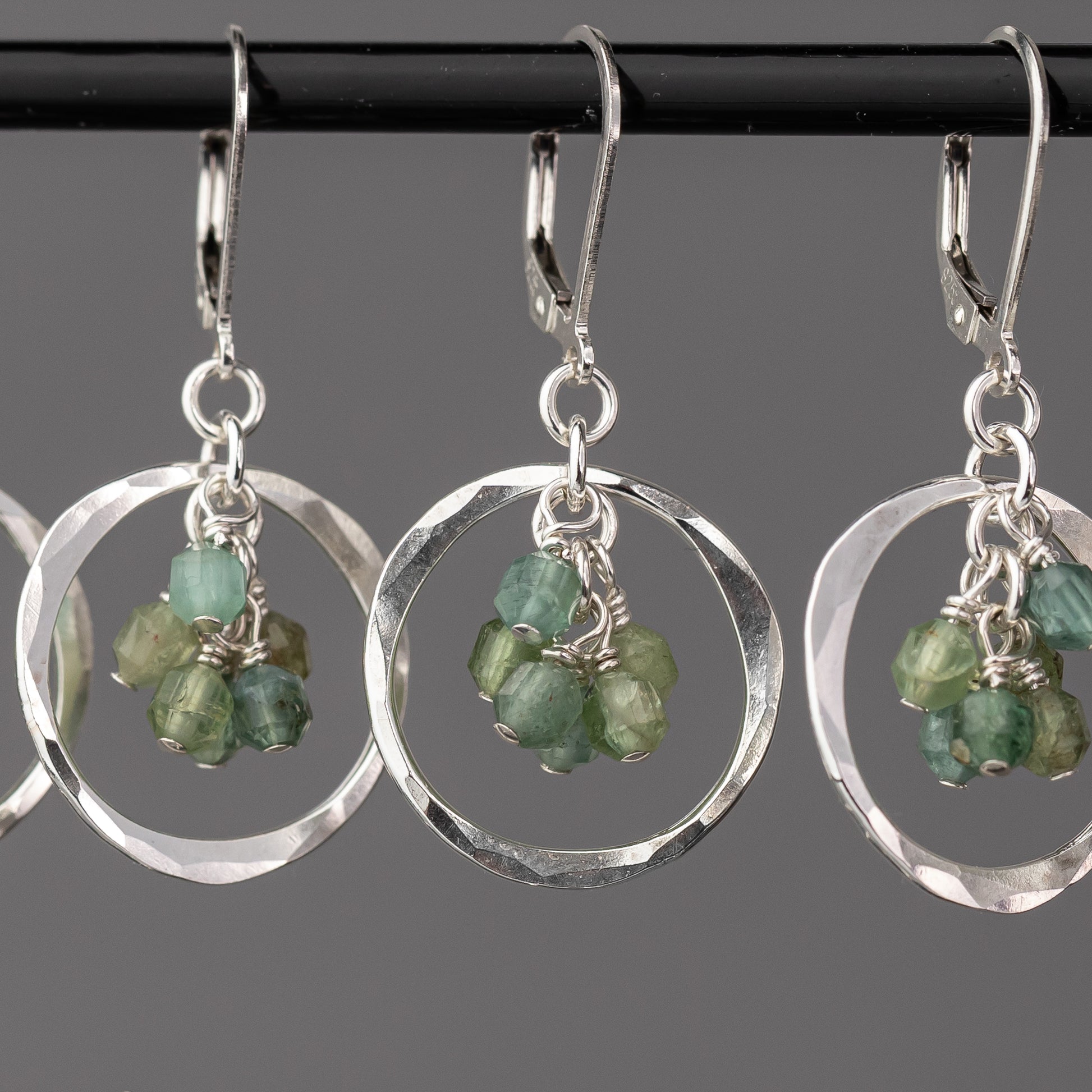 Hammered silver earrings with green apatite gemstones on a gray background