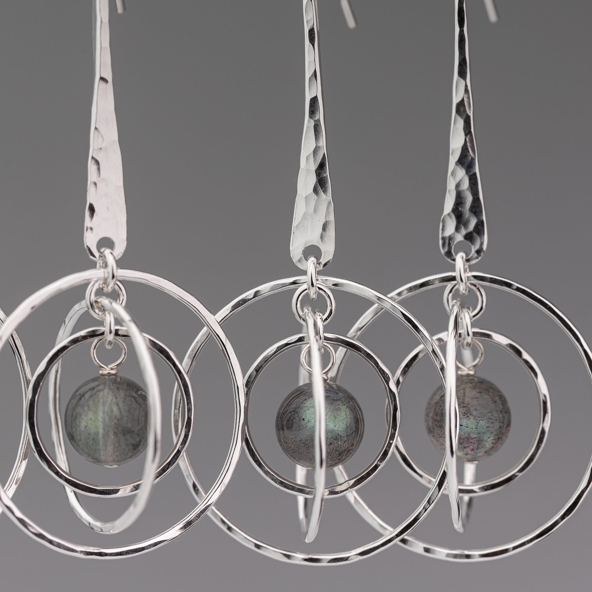 Handmade sterling silver earrings with circular designs and a central labradorite stone on a gray background