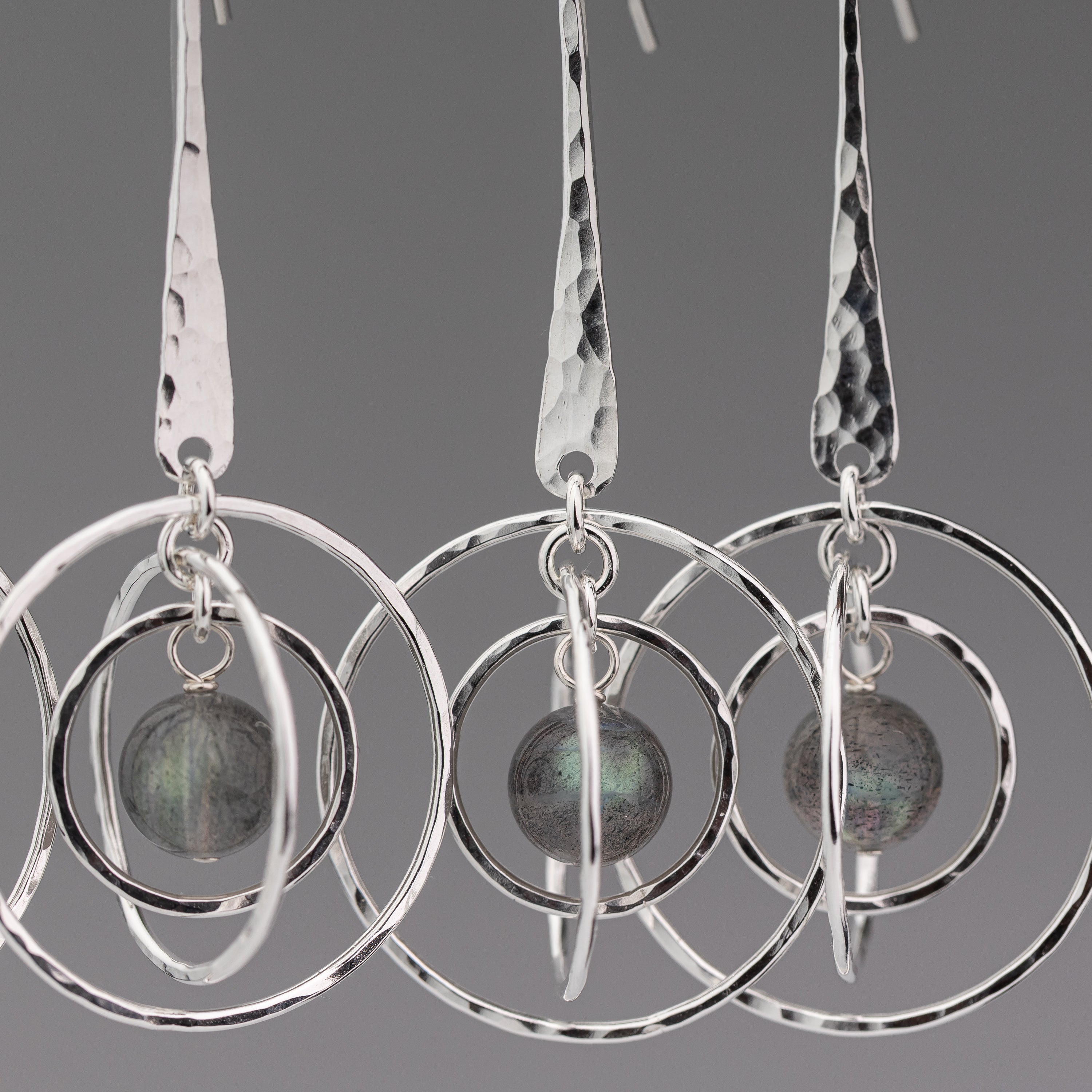 Handmade sterling silver earrings with circular designs and a central labradorite stone on a gray background