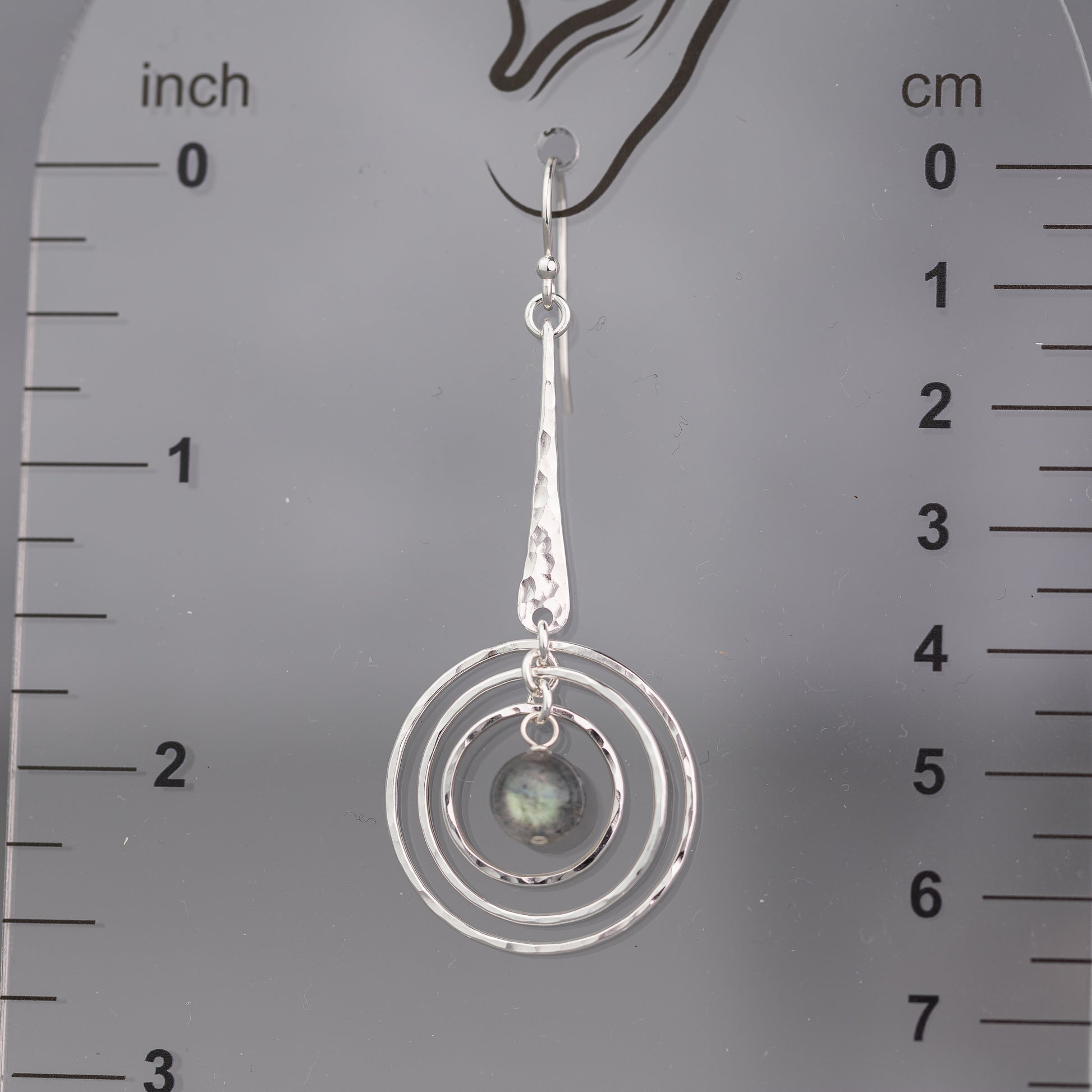 handmade sterling silver labradorite earring with circular design on a ruler for scale.  The silver is hand hammered or texture and polished to a high shine