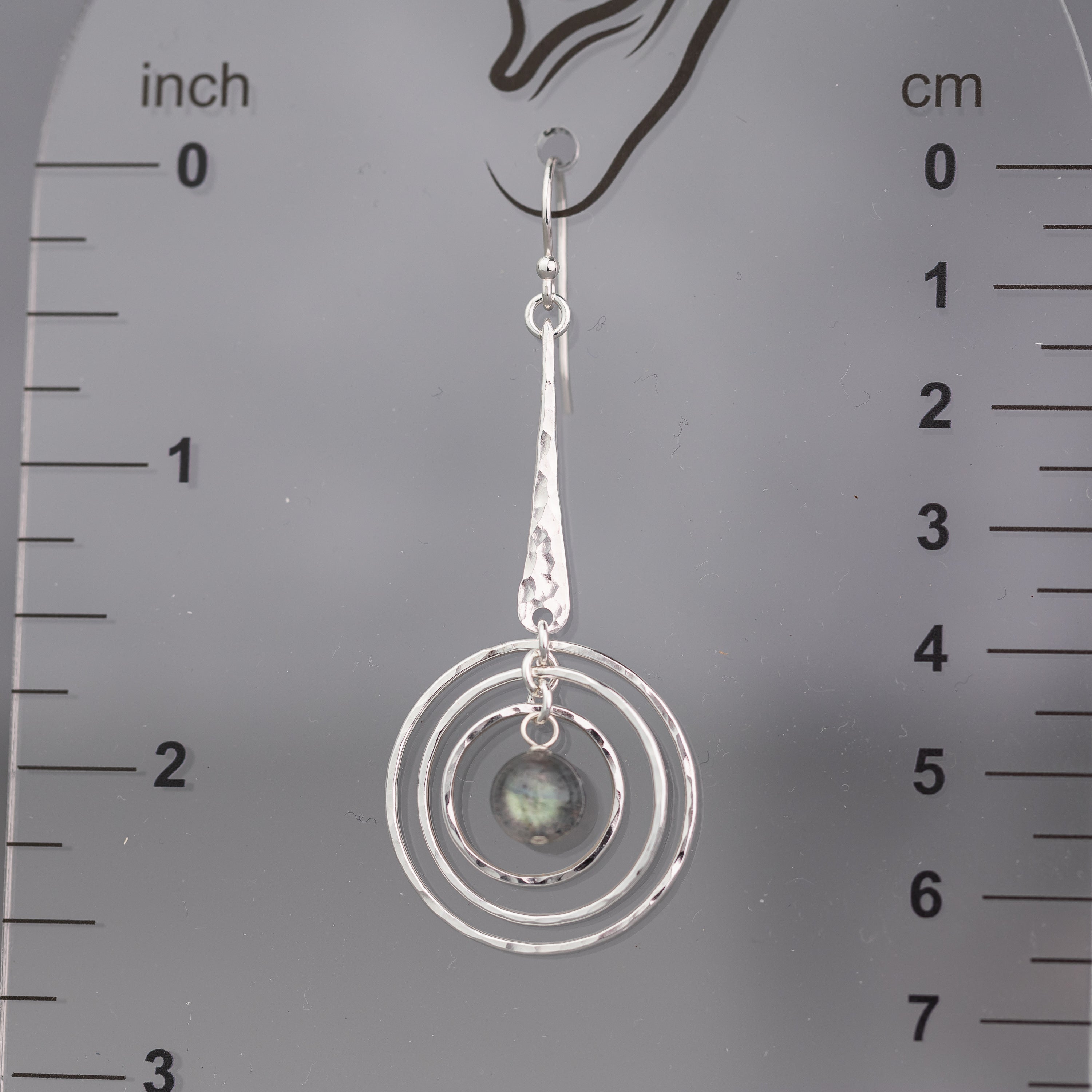 handmade sterling silver labradorite earring with circular design on a ruler for scale.  The silver is hand hammered or texture and polished to a high shine
