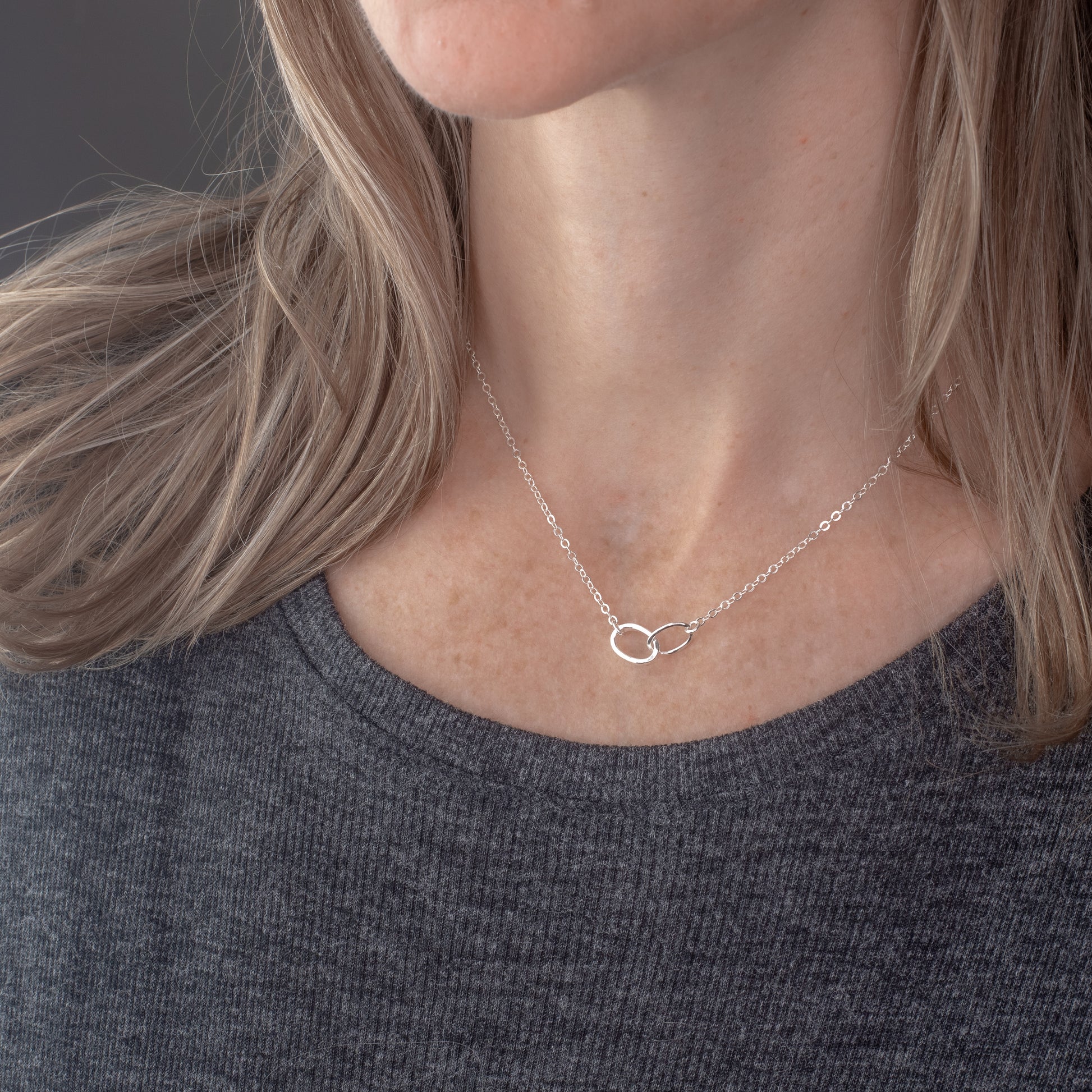 Person wearing a delicate silver necklace with a small pendant against a neutral background