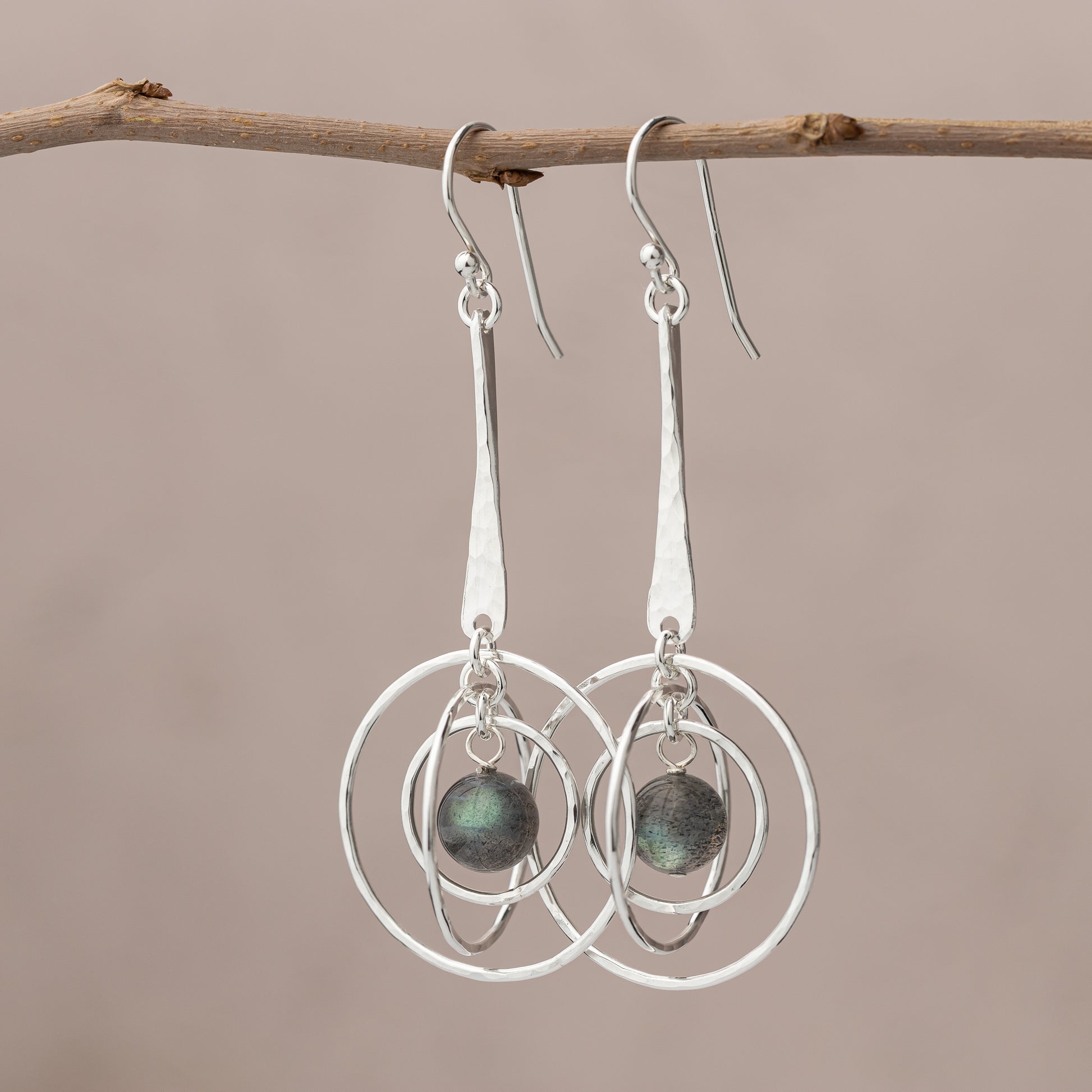Sterling Silver Labradorite earrings with circular designs hanging from a branch against a beige background