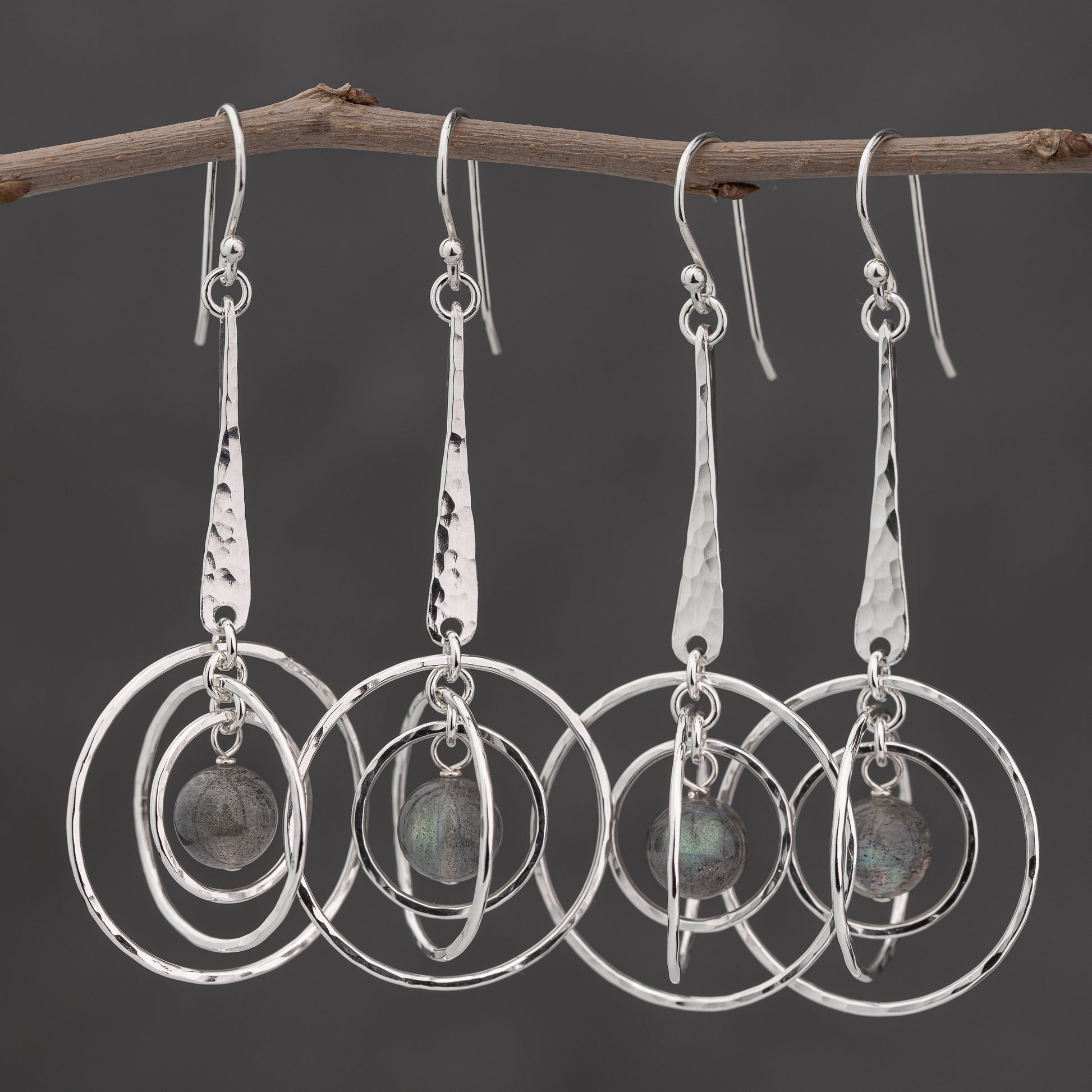 Handmade Argentium silver earrings with circular orbit designs hanging from a branch against a dark background