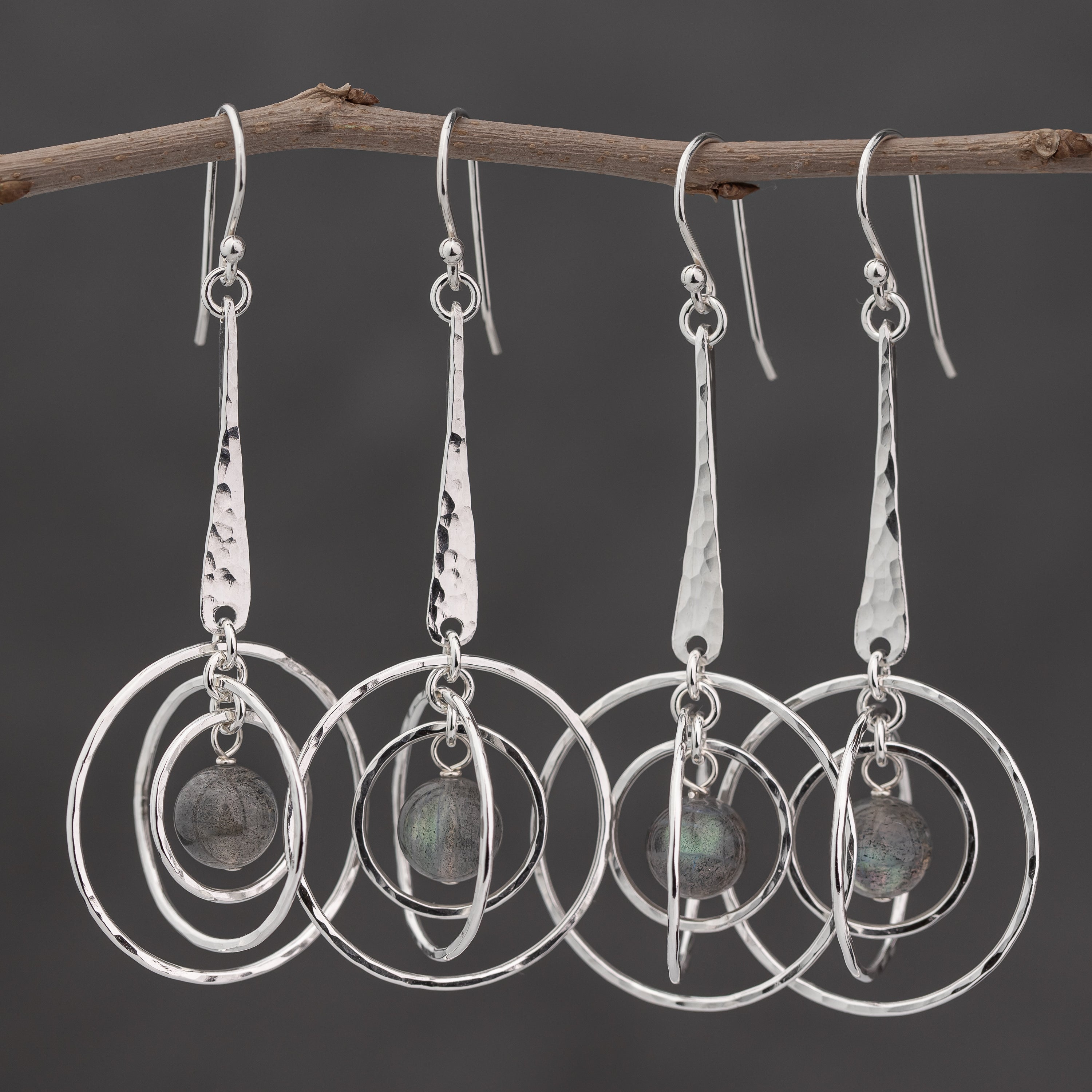 Handmade Argentium silver earrings with circular orbit designs hanging from a branch against a dark background