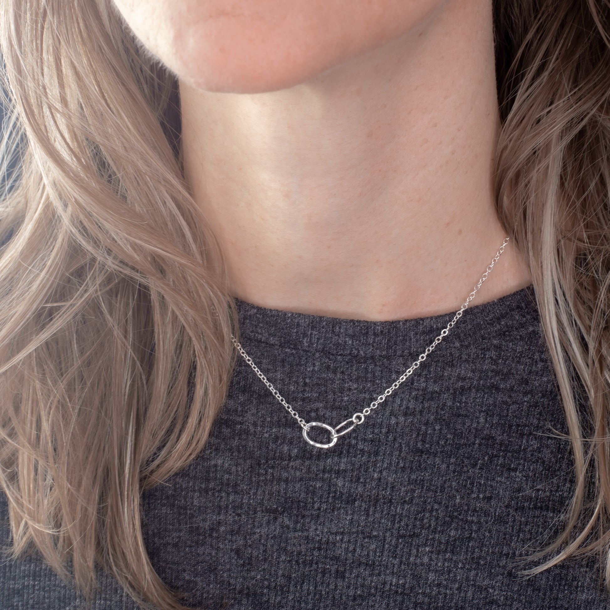 Person wearing a delicate silver necklace with an oval linked thick and thin pendant.