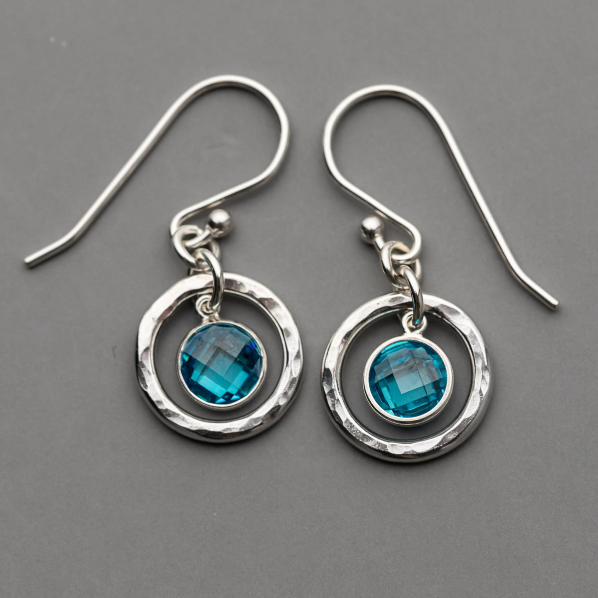 hammered sterling silver circle dangle earrings with blue checkerboard cut cubic zirconia gemstones shown on a gray background