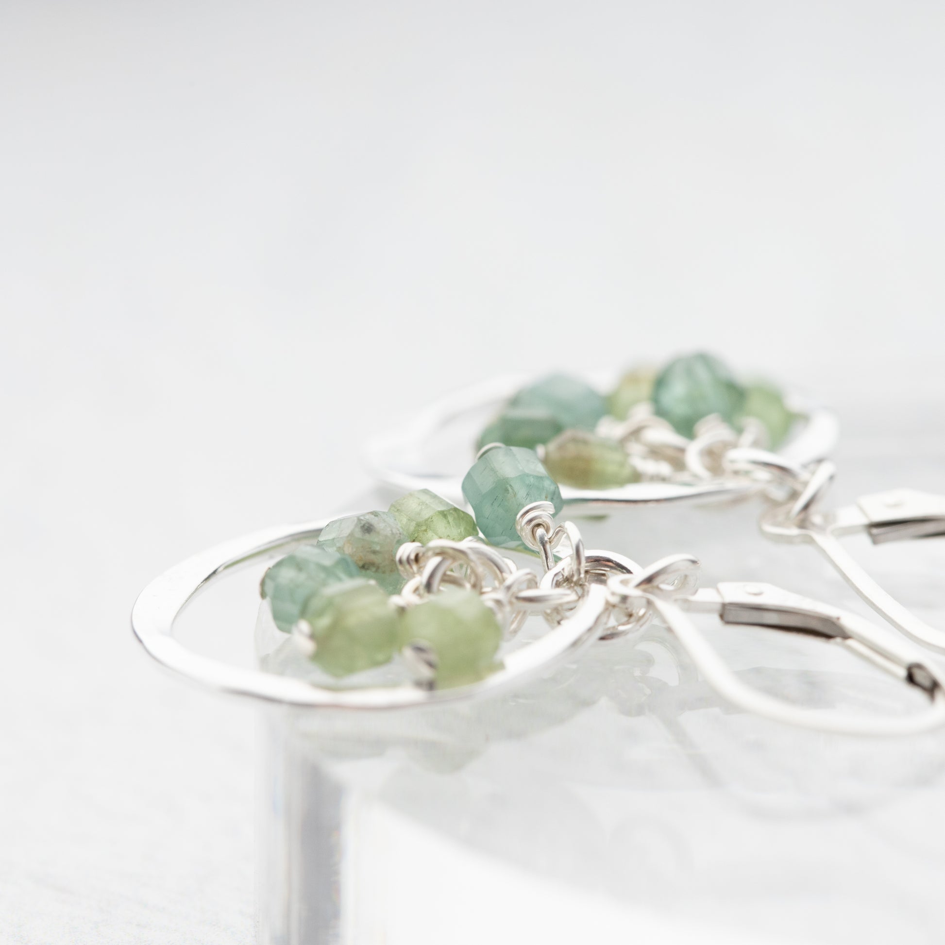 Silver earrings with green apatite gemstones on a white background