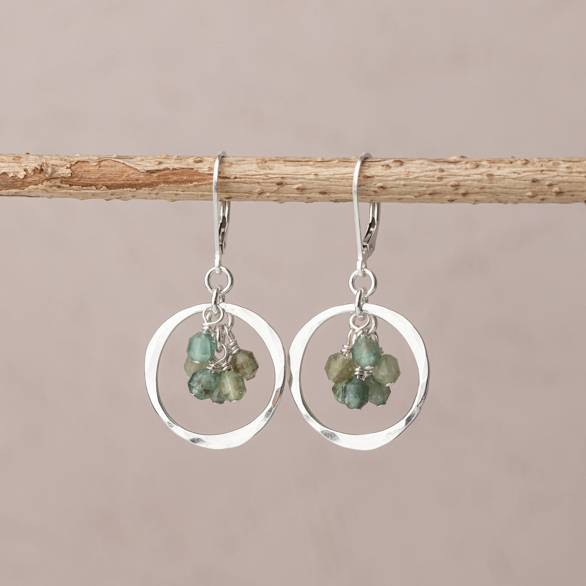 Handmade sterling silver earrings with green gemstones on a branch against a beige background