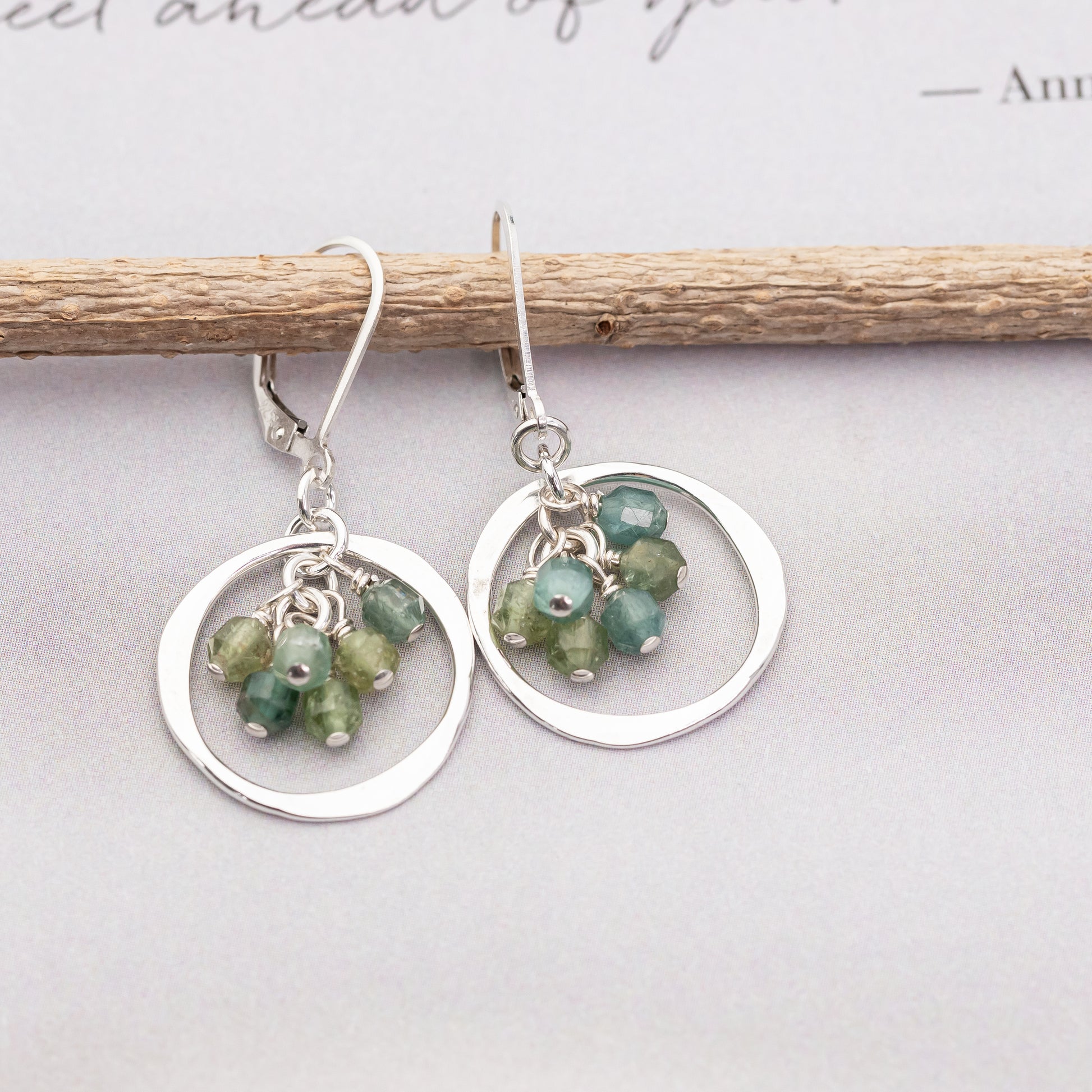 Handmade silver earrings with green and blue apatite gemstones clustered together on a light gray background