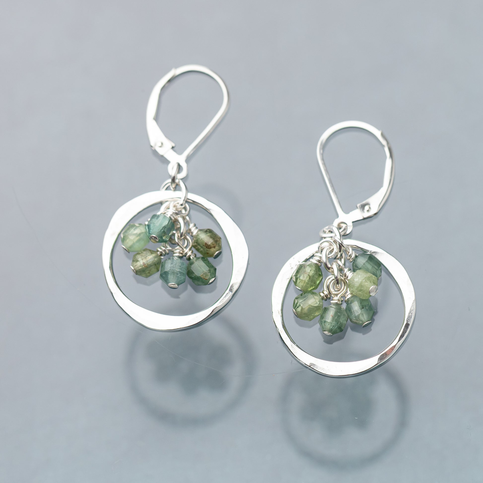 Hammered silver circle earrings with green gemstones on a gray background