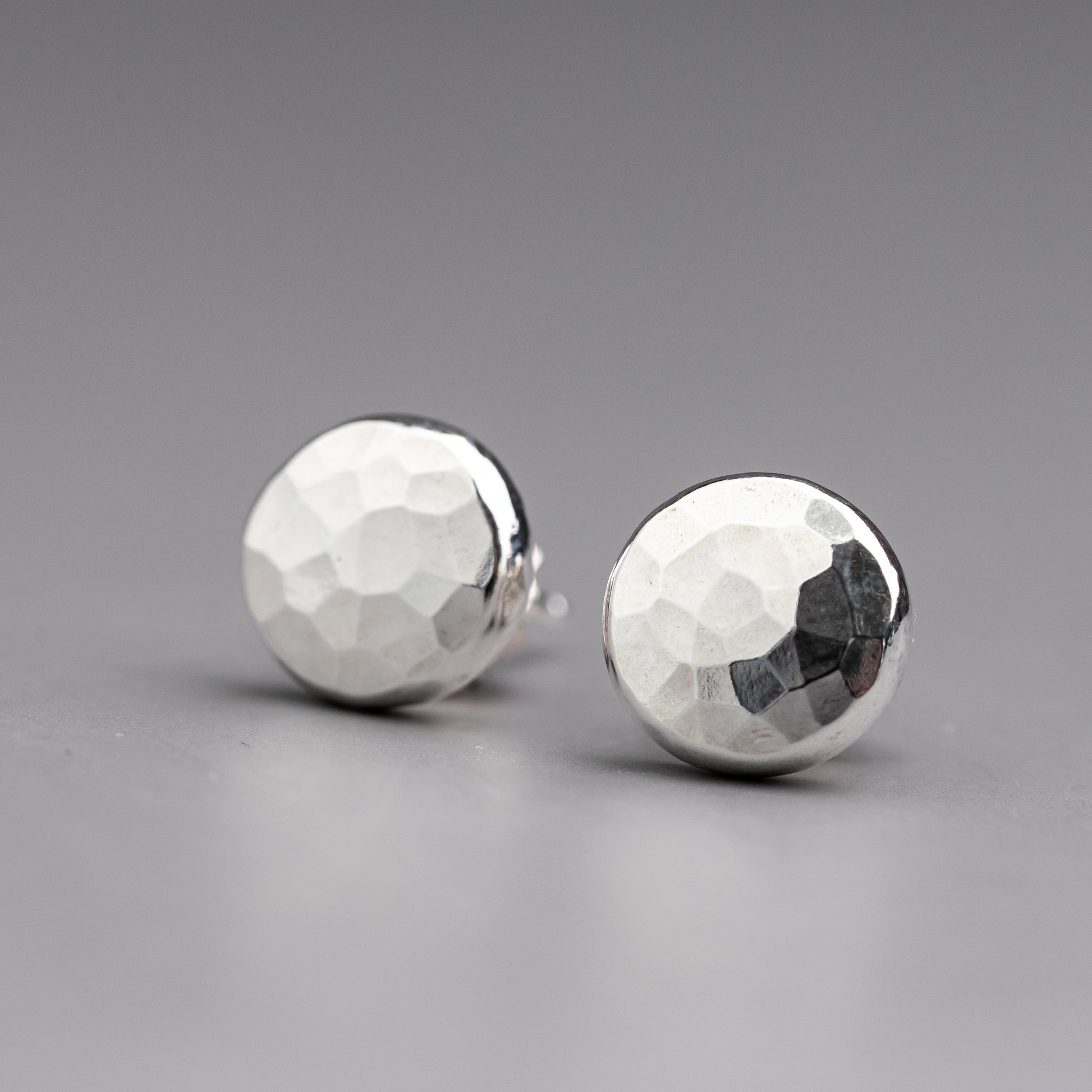 Close up of a pair of handmade sterling silver stud earrings with a unique Hamer faceted texture on the surface.