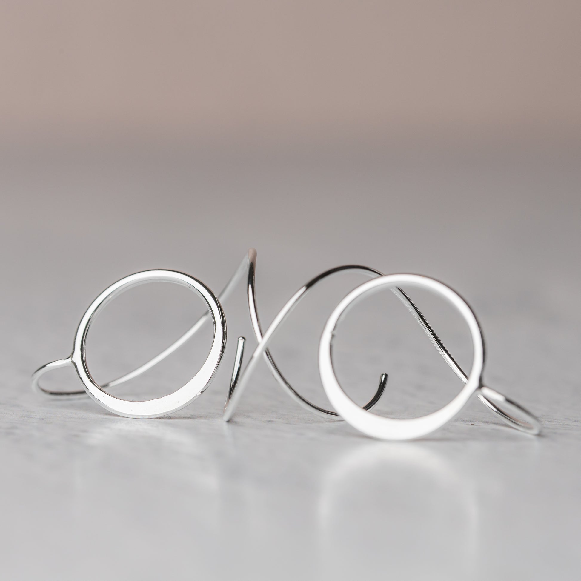 Sterling Silver circular earrings on a reflective surface with a gradient background