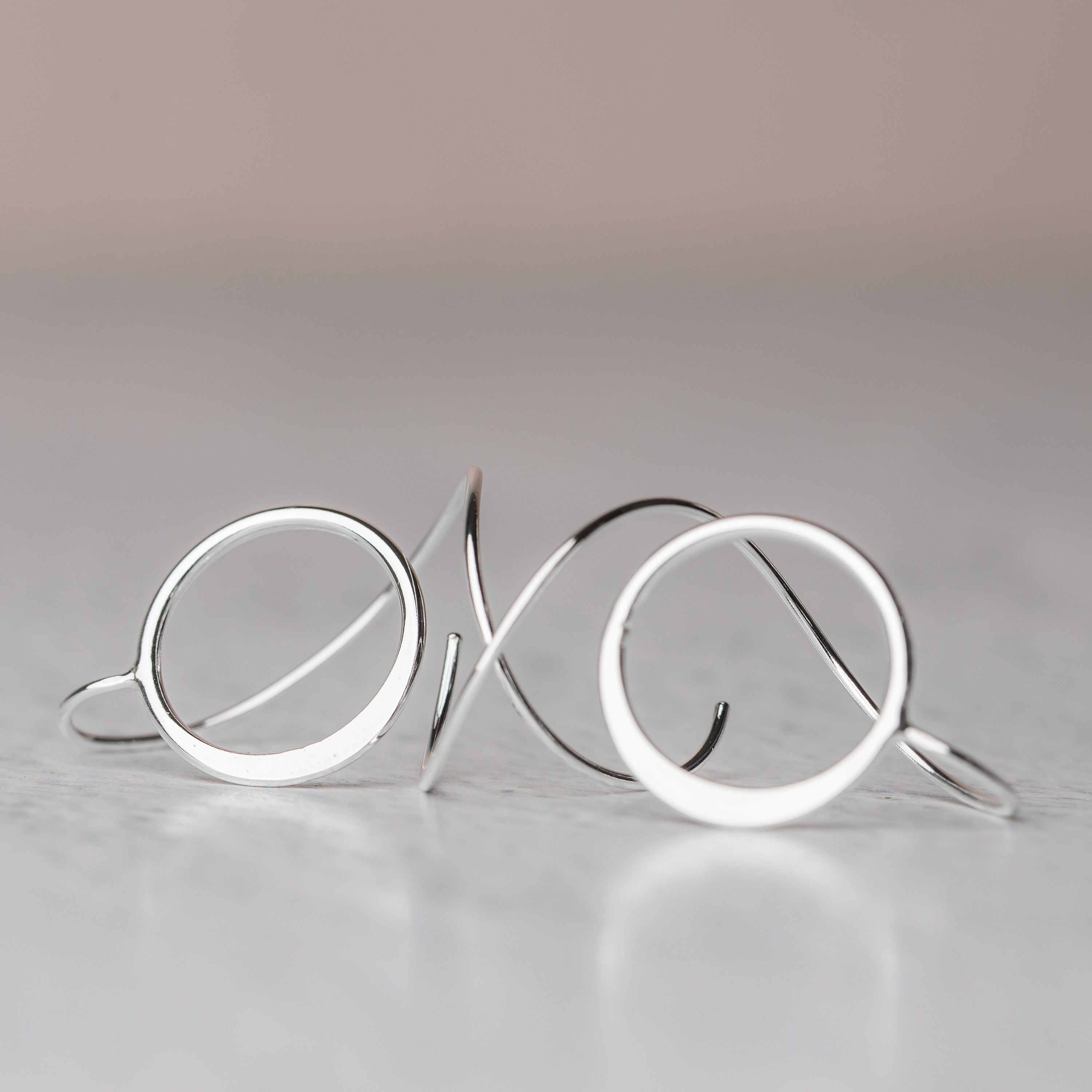 Sterling Silver circular earrings on a reflective surface with a gradient background