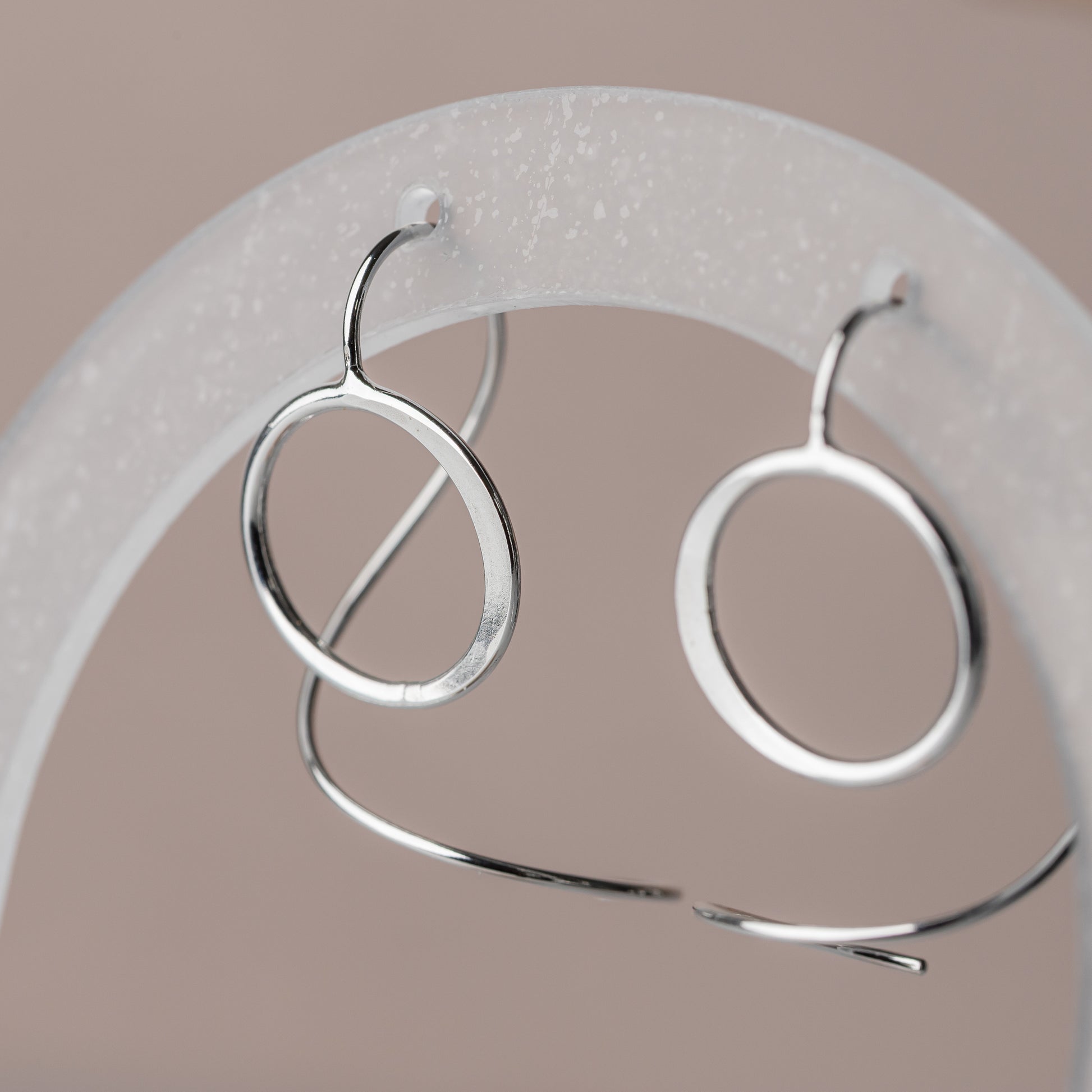 Silver circle threader earrings on a white stand against a beige background