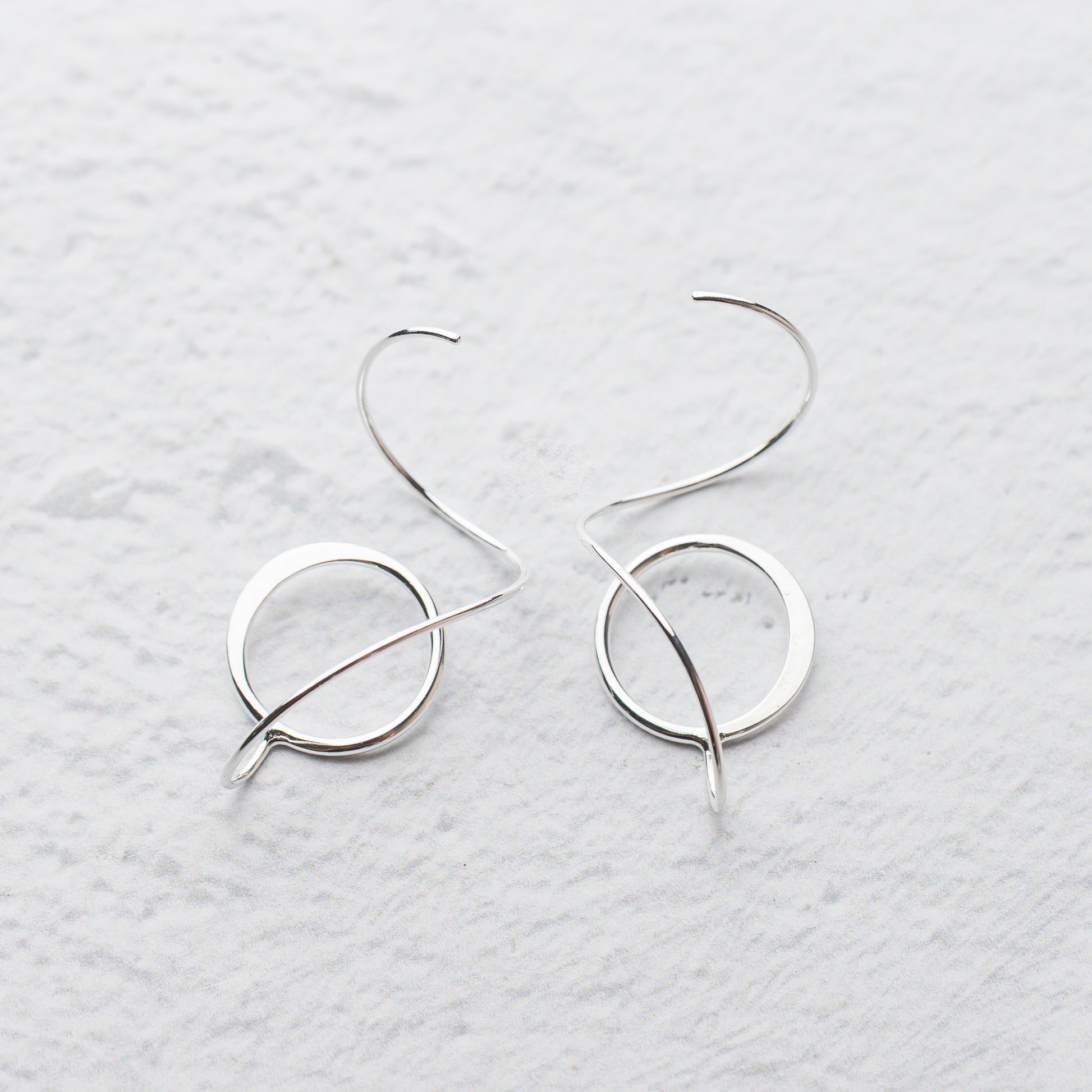 Pair of handmade silver hoop earrings on a light gray textured background
