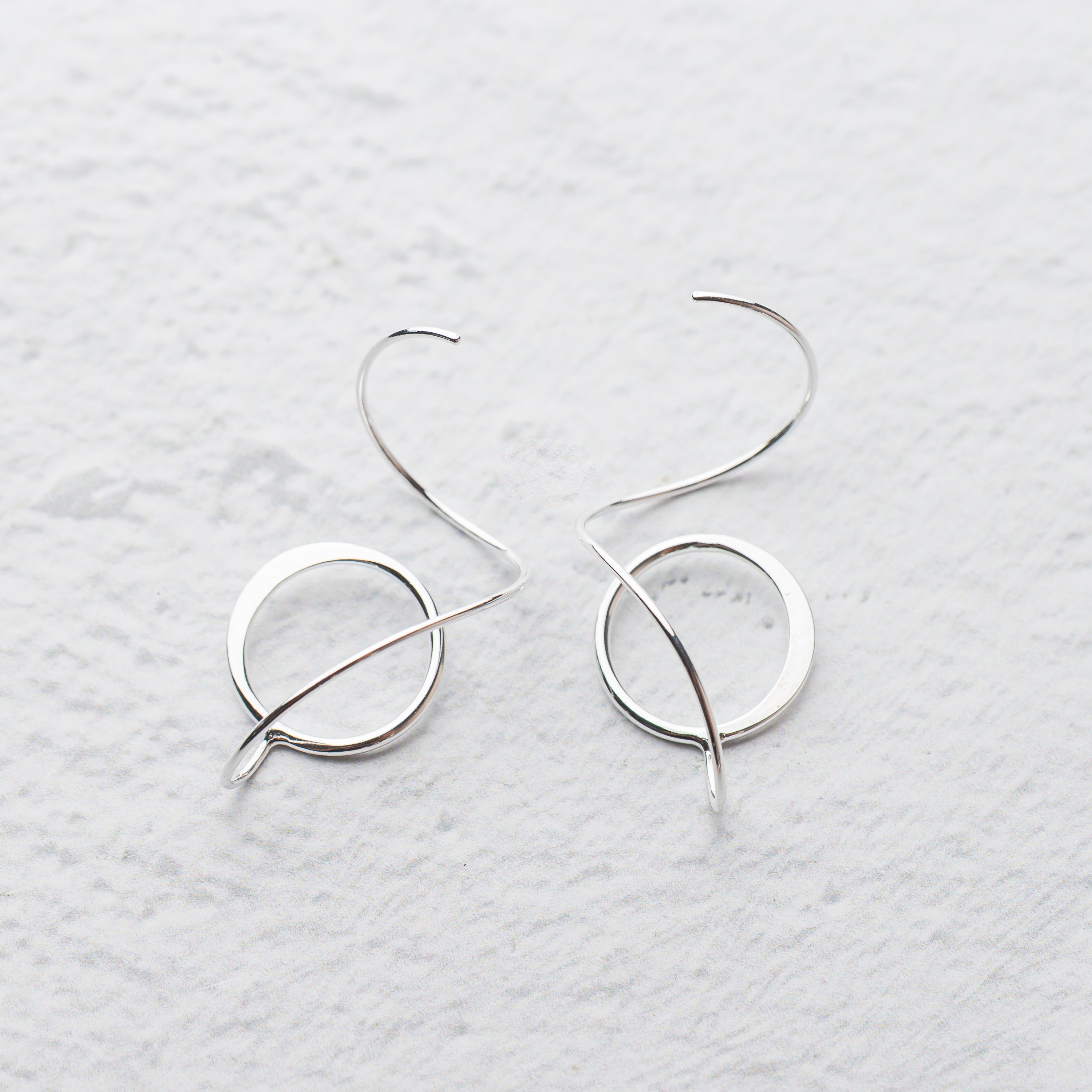 Pair of handmade silver hoop earrings on a light gray textured background