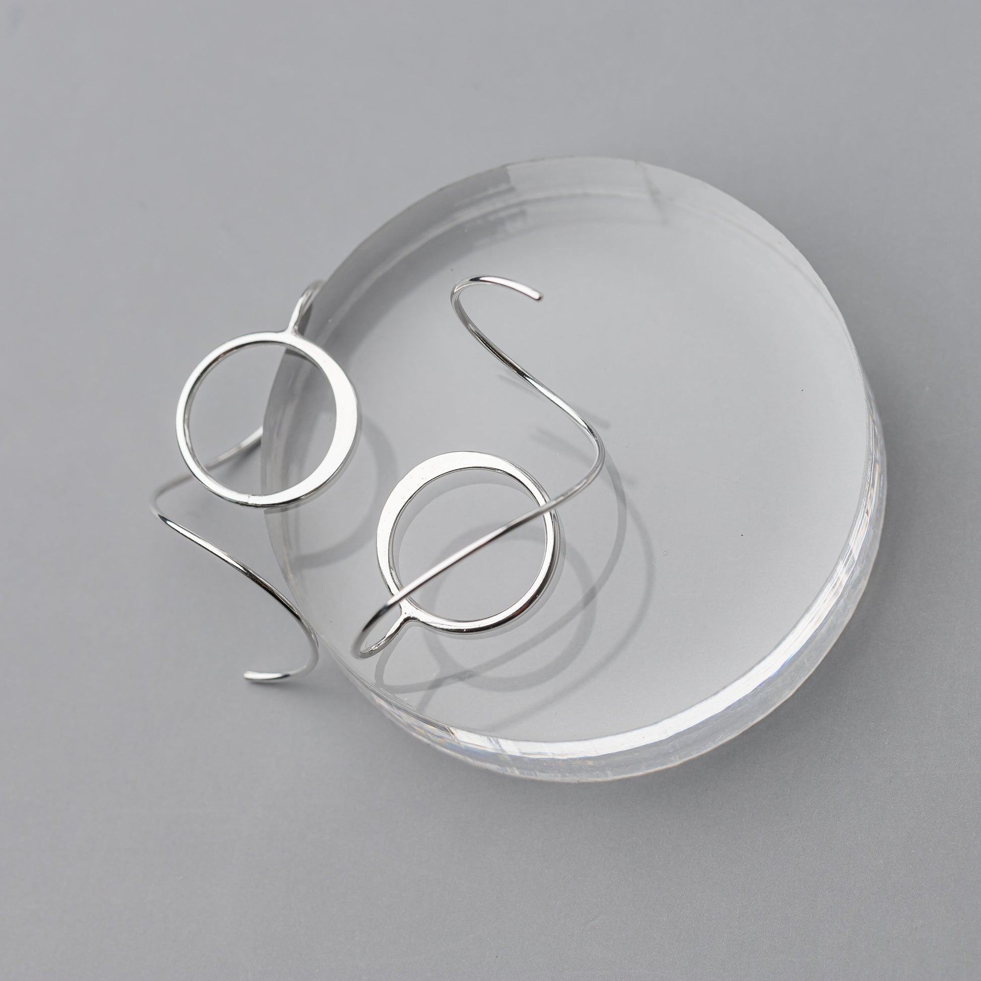 Silver spiral earrings on a clear round stand against a gray background