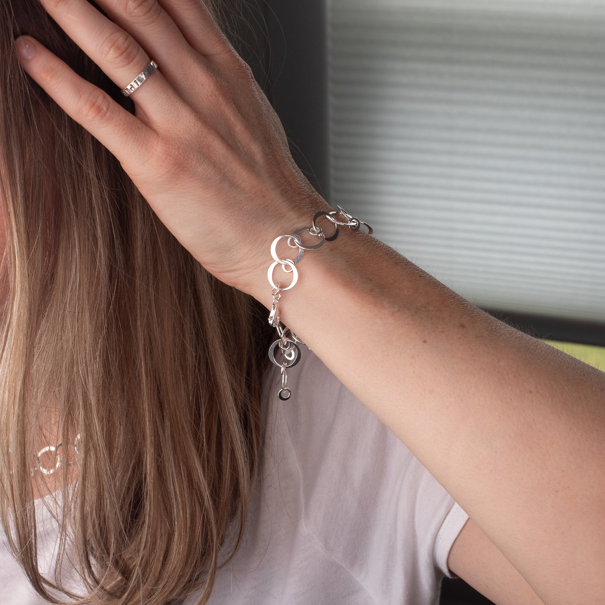 Close-up of a hand wearing a handmade sterling silver bracelet with circle charms, blurred background