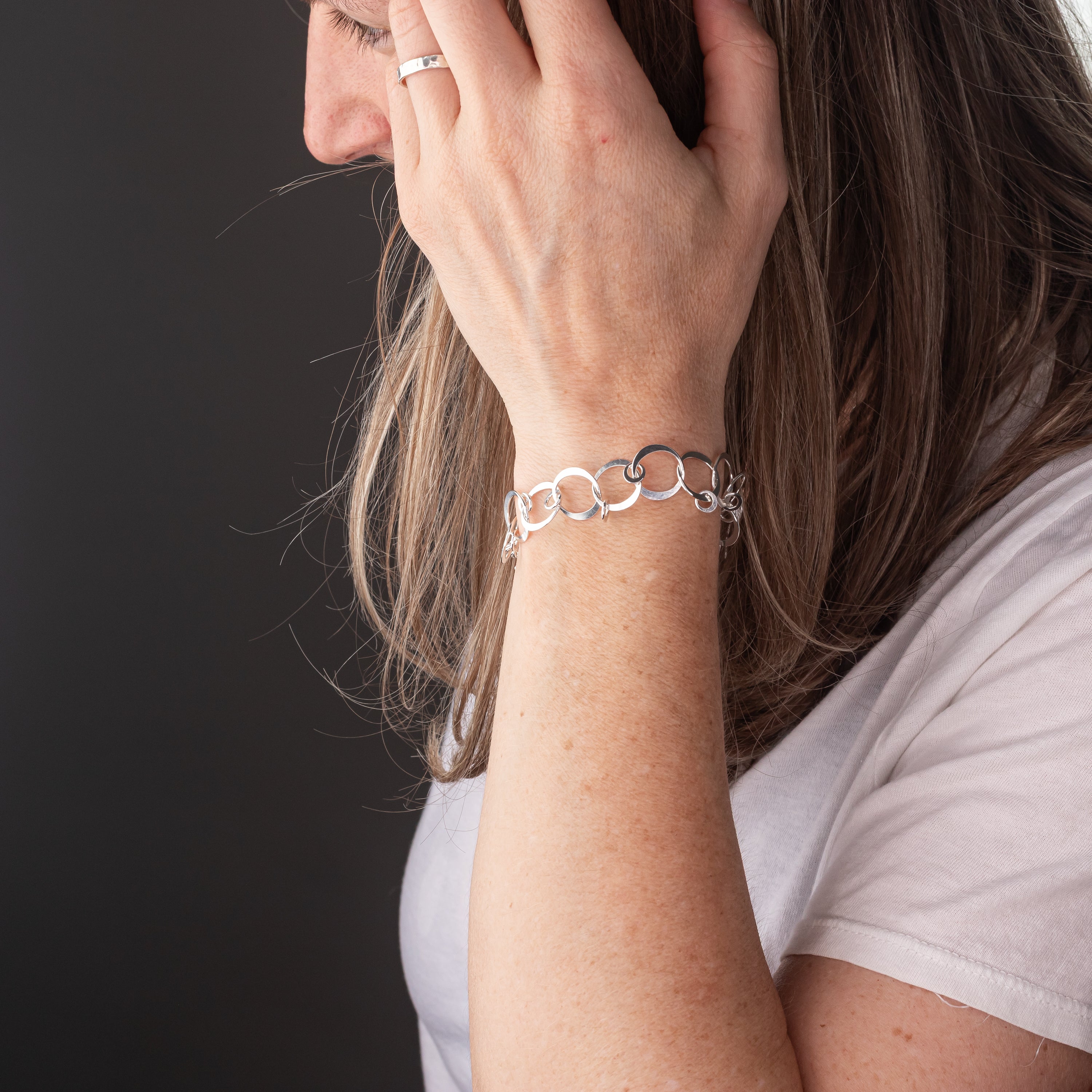 Person wearing a sterling silver chain bracelet on a dark background.  The chain is handmade with silver circles and charms