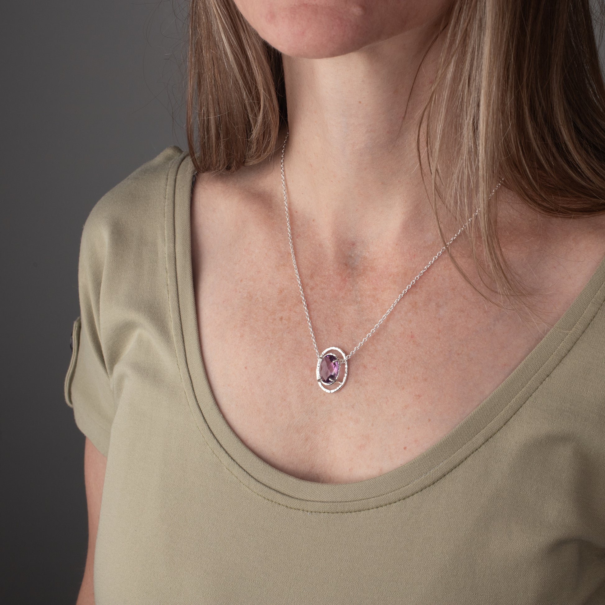 Person wearing a necklace with a pendant against a neutral background