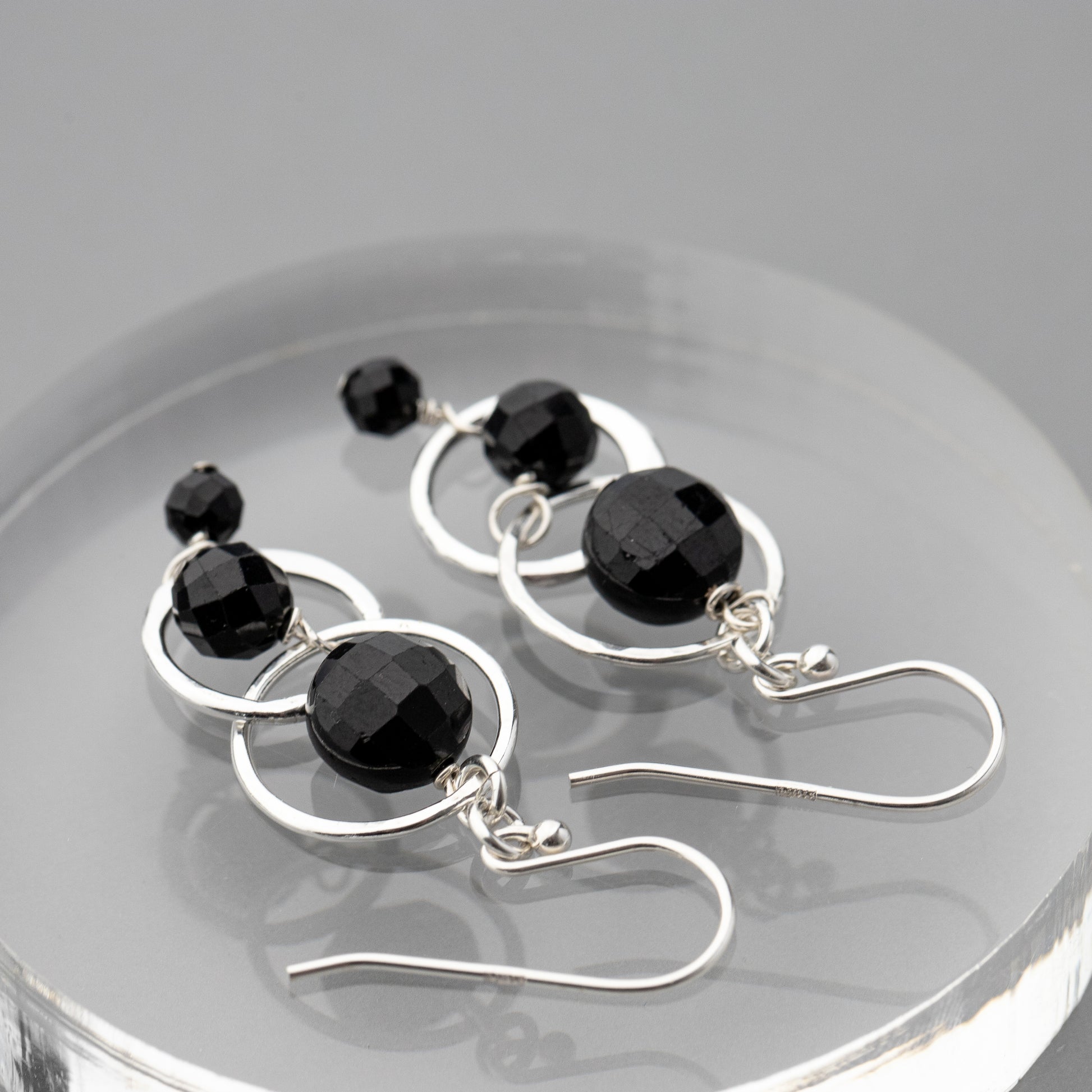 Black tourmaline and sterling silver handmade earrings on a reflective surface