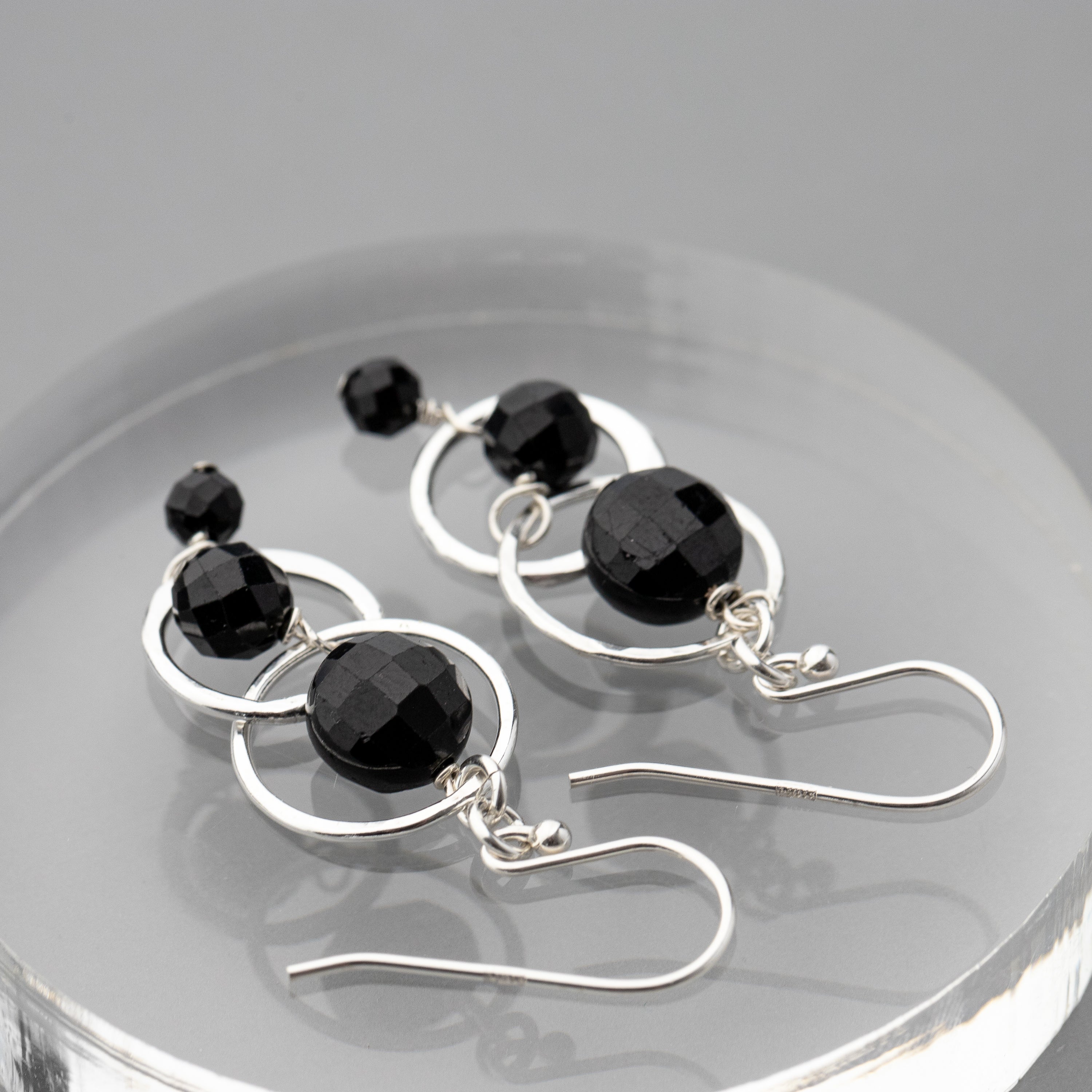 Black tourmaline and sterling silver handmade earrings on a reflective surface
