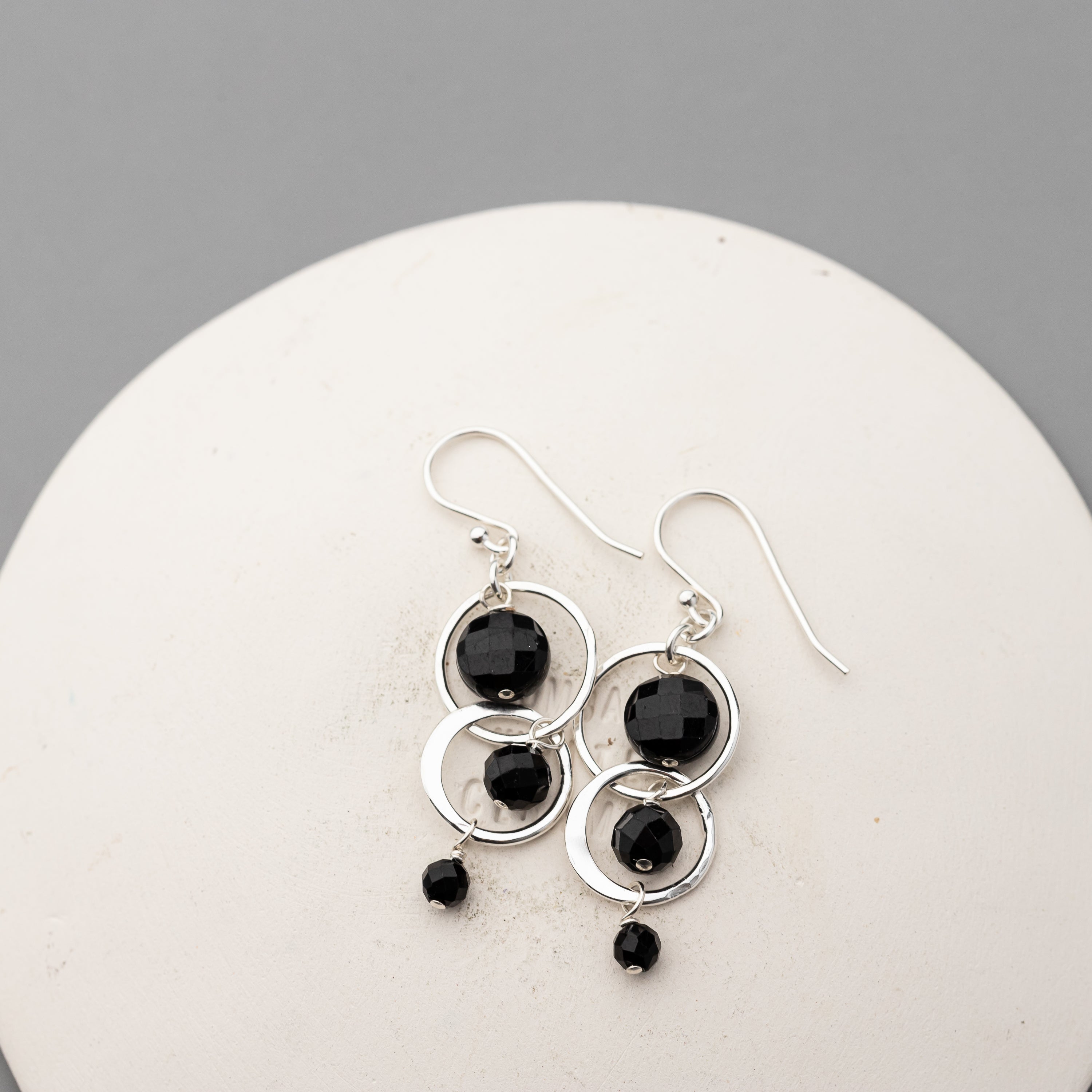 sterling silver earrings with black tourmaline beads on a white stone surface